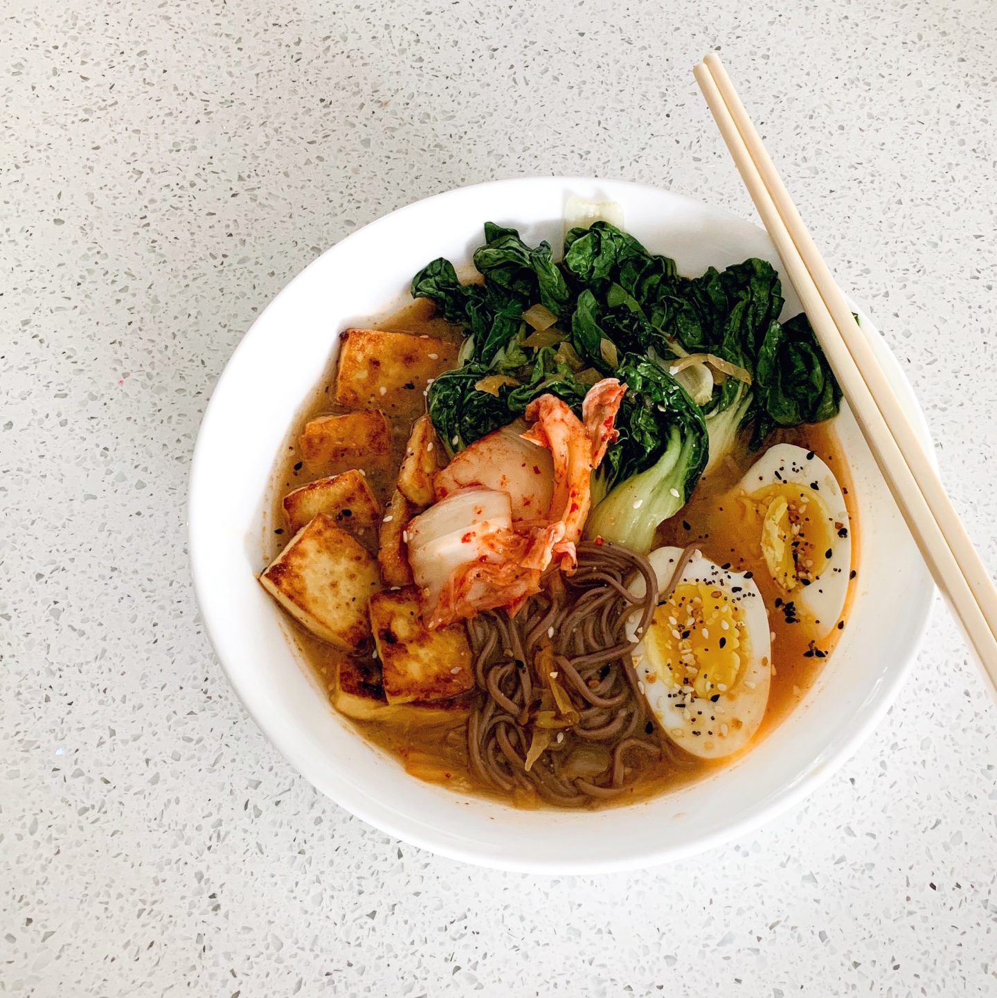 a bowl full of noodles, tofu, kimchi, bok choy, a medium boiled egg,, all sitting in a hearty broth - a part of hobbies I'm taking part in during a low buy year