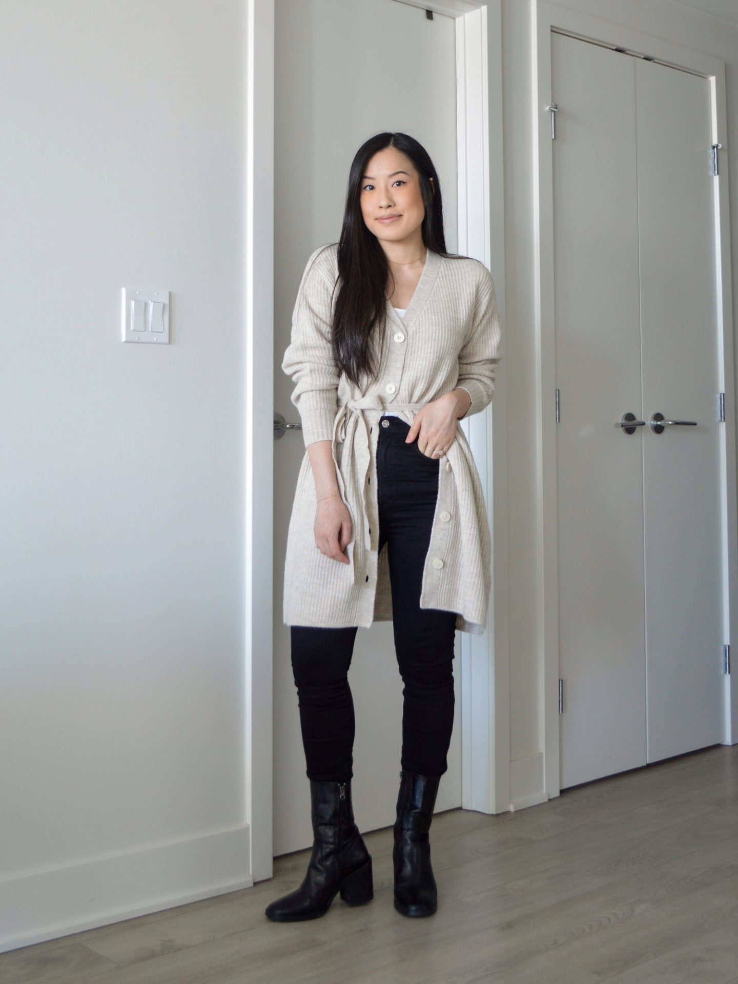 Sharon of Her Simple Sole is wearing the Frank and Oak The Recycled Wool Cardigan Dress buttoned halfway down with a white tank top, black skinny jeans and black ankle boots.