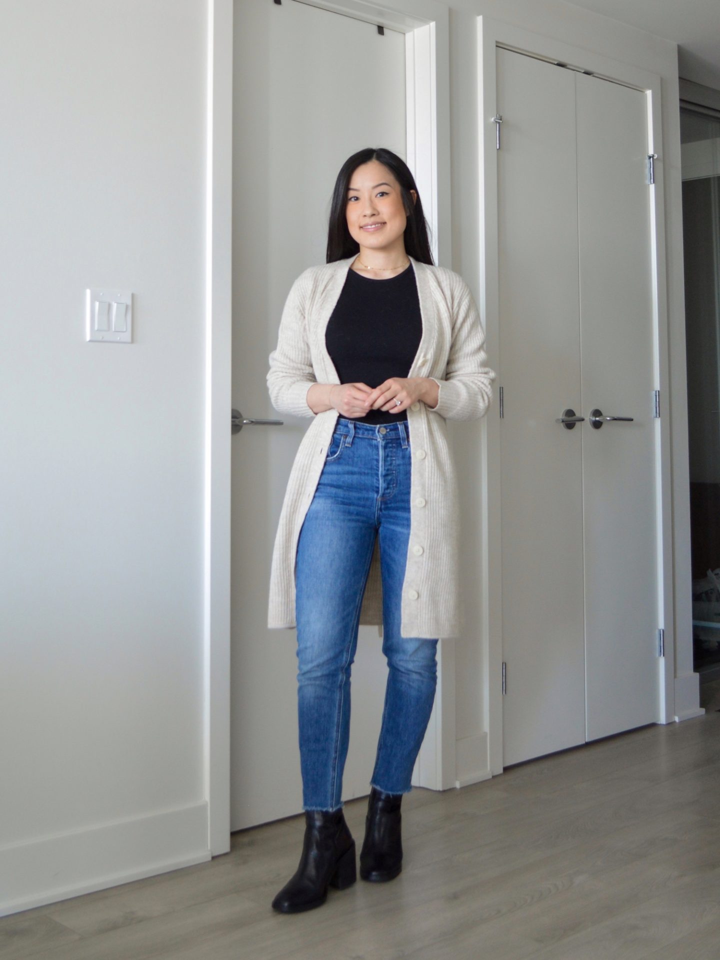 Sharon of Her Simple Sole is wearing the Frank and Oak The Recycled Wool Cardigan Dress opened with a black long sleeve tshirt, blue slim jeans and black ankle boots.