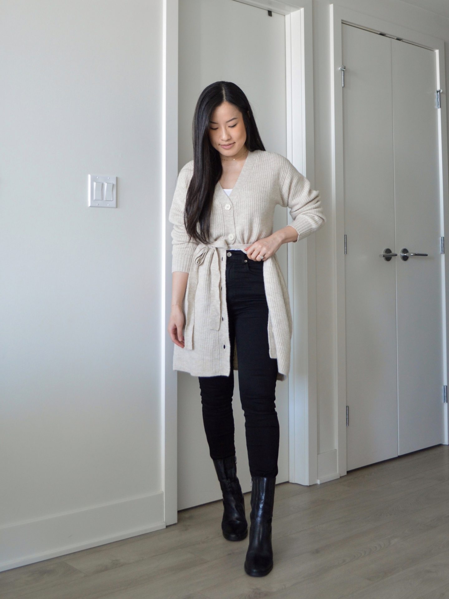 Sharon of Her Simple Sole is wearing the Frank and Oak The Recycled Wool Cardigan Dress buttoned halfway down with a white tank top, black skinny jeans and black ankle boots.