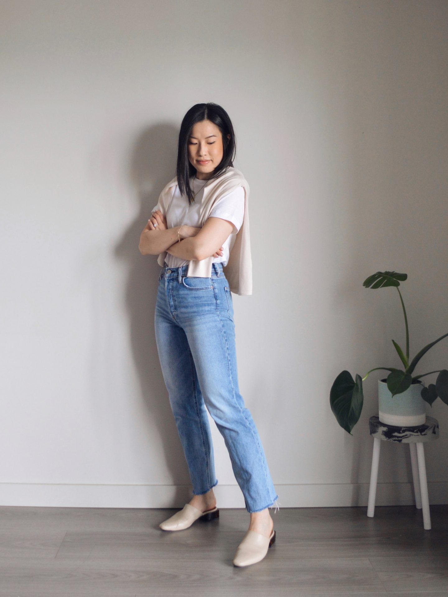 Outfit details: white t-shirt, merino wool sweater over shoulders, blue straight leg jeans, cream mules