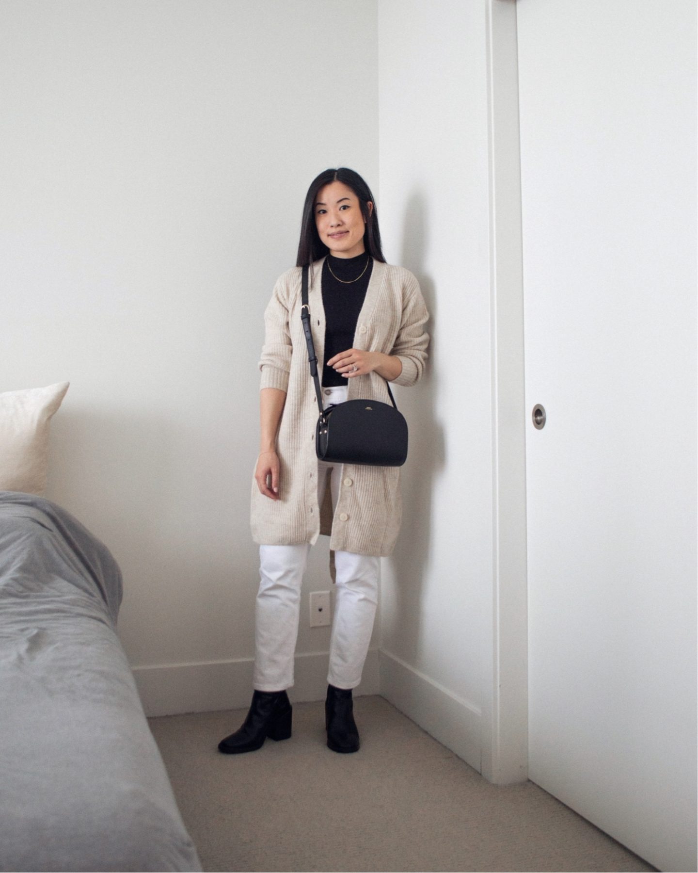 Outfit details - long neutral cardigan, black mock neck tank top, white straight leg jeans, black mid-calf boots, black half moon bag