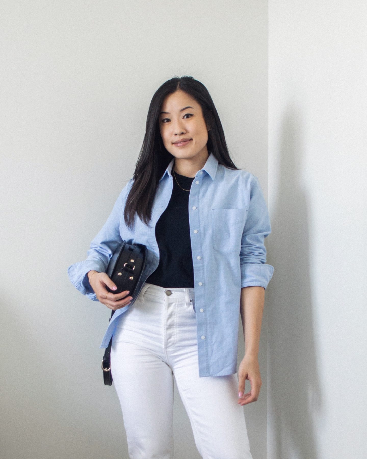 Outfit details - blue relaxed oxford shirt, classic black t-shirt, white straight leg means, black half moon bag