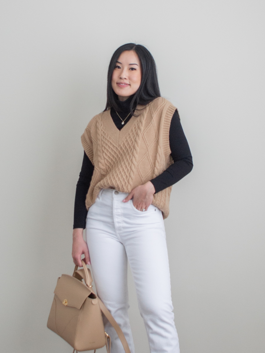 Her Simple Sole detailed outift photo featuring camel knit sweater vest layered over a black turtleneck top, white straight leg jeans, black chunky combat boots, Oleada Wavia bag in Champagne
