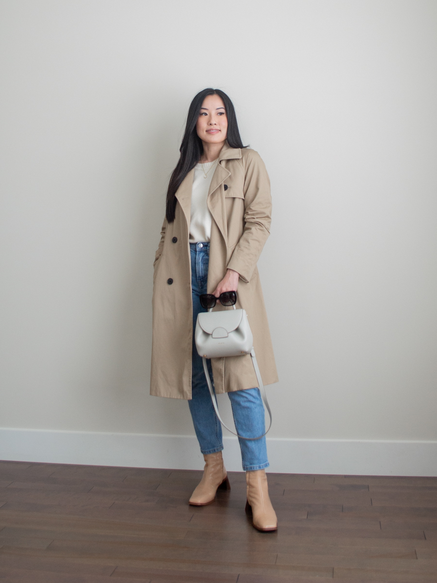 Her Simple Sole outfit photo featuring a classic tan trench coat, a cream cotton sweater, blue straight leg jeans, beige ankle boots, an off-white crossbody bag, and a pair of square frame sunglasses