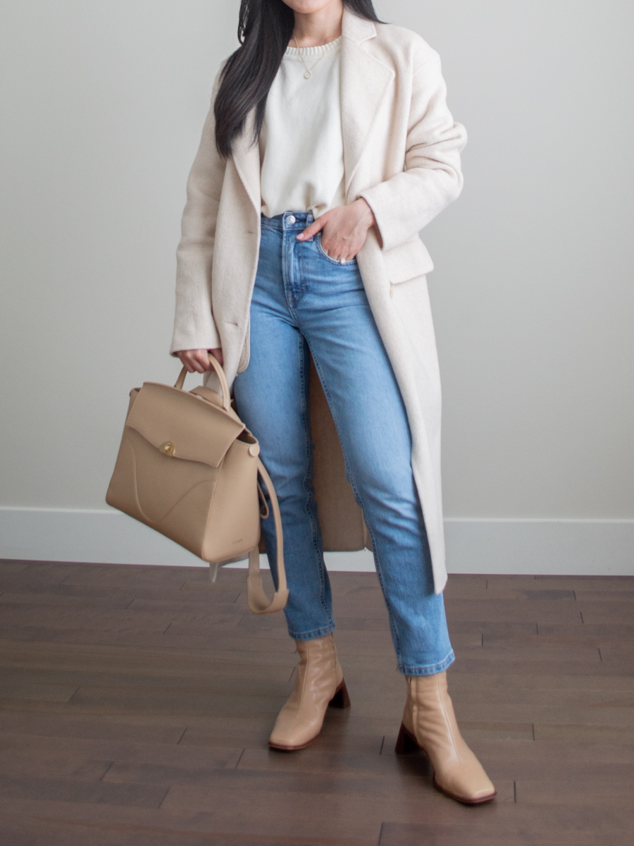 Her Simple Sole outfit photo featuring cream wool coat, blue straight leg jeans, cream cotton sweater, beige ankle boots, Oleada Wavia bag in Champagne
