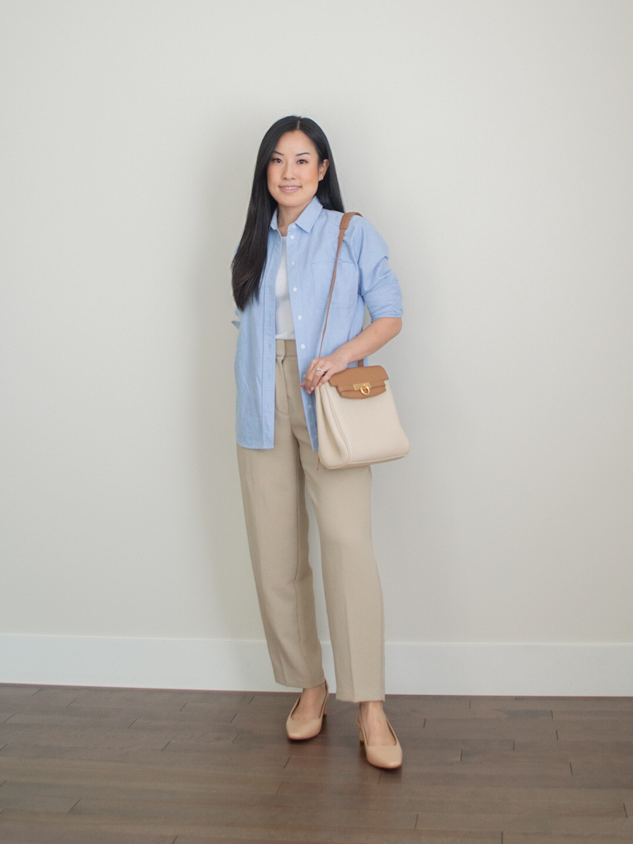 outfit photo of a blue relaxed oxford shirt styled with beige trousers, and heels, and a bag from Parisa Wang, intentional gifts under $100