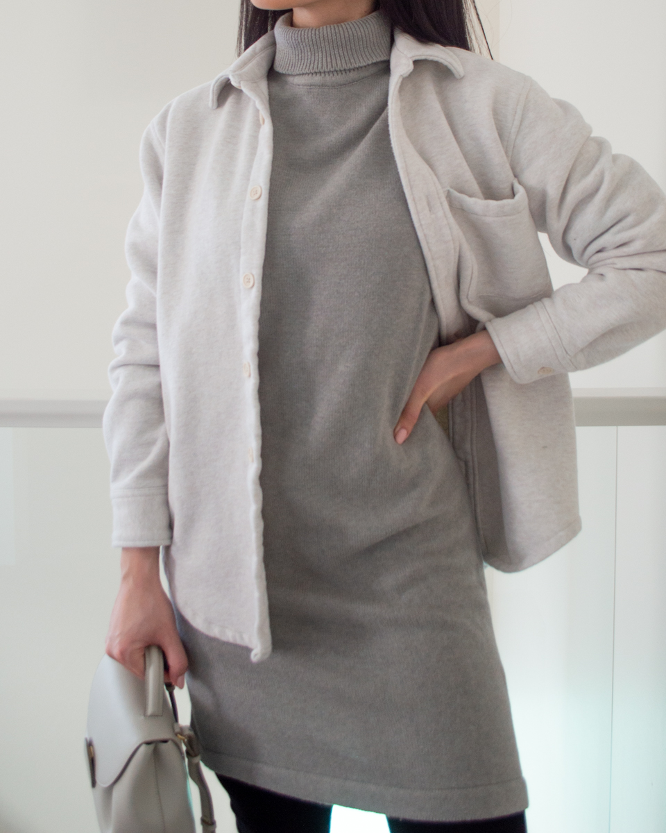 Close-up shot of Sharon of Her Simple Sole wearing a smart casual outfit featuring a grey sweater dress, white fleece shirt jacket, and black leggings while holding a small cream bag