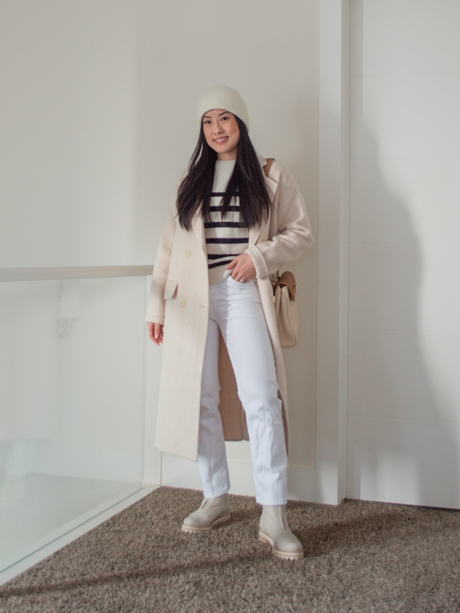 Sharon of Her Simple Sole wears a Cream Chunky Boots Outfit featuring a striped sweater, wool coat, white straight leg jeans, cream beanie, and two-toned crossbody bag