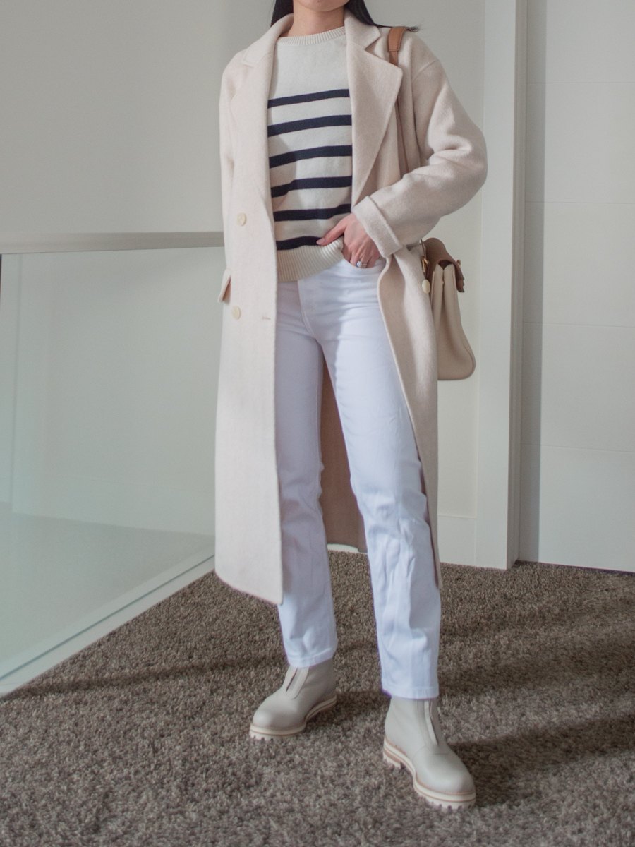 Sharon of Her Simple Sole wears a Cream Chunky Boots Outfit featuring a striped sweater, long cream coat, white jeans and two-toned crossbody bag