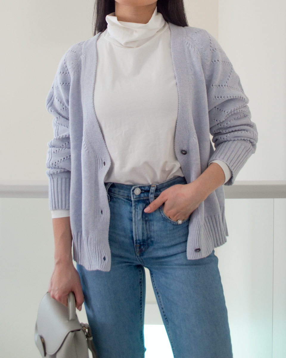 Close-up shot of Sharon of Her Simple Sole wearing a warm winter outfit featuring a knit cardigan, turtleneck top, and straight leg jeans while holding a crossbody bag