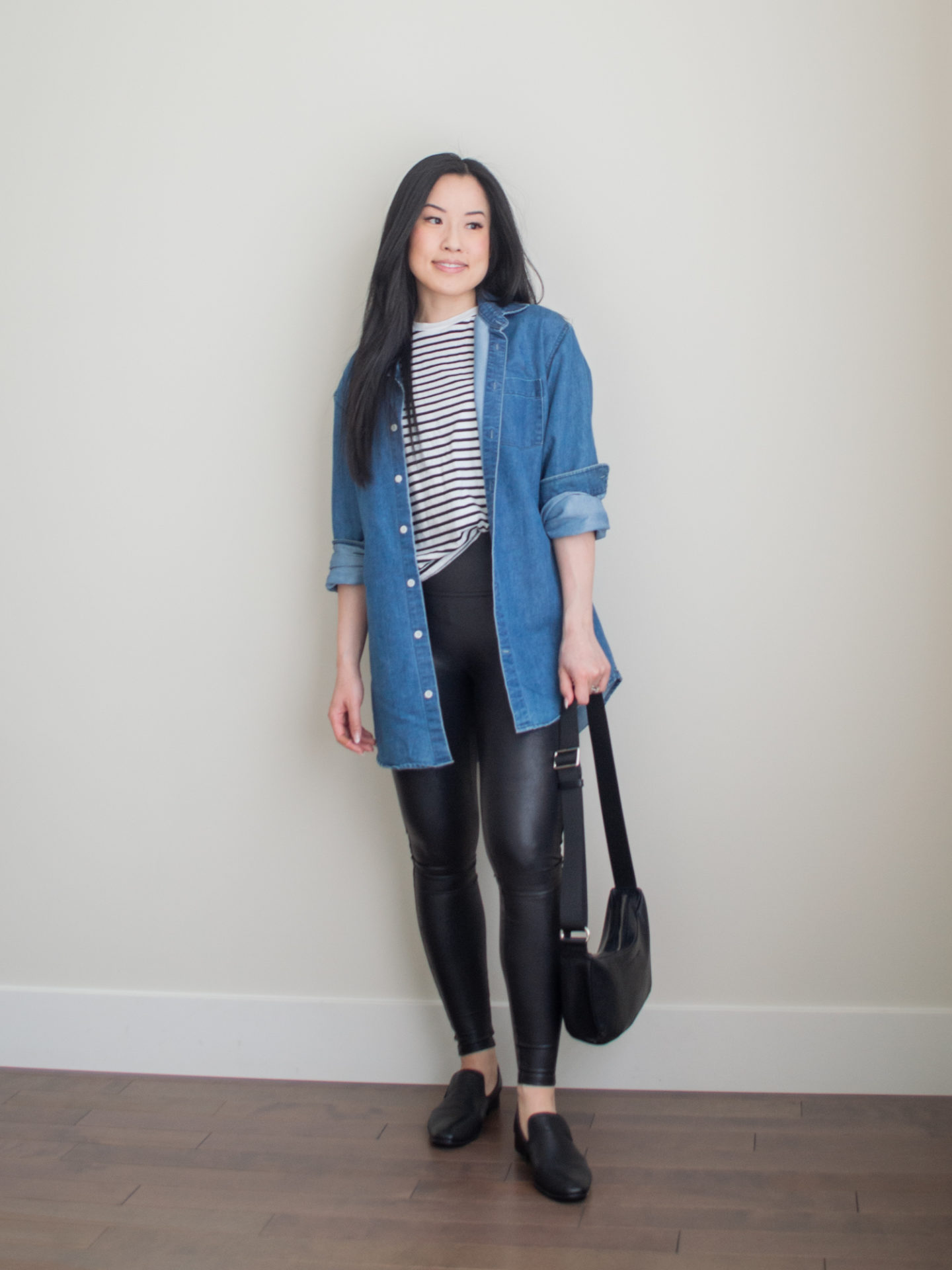 Casual spring outfit idea: slouchy crossbody bag, oversized denim shirt, black and white striped t-shirt, faux leather leggings, classic black loafers