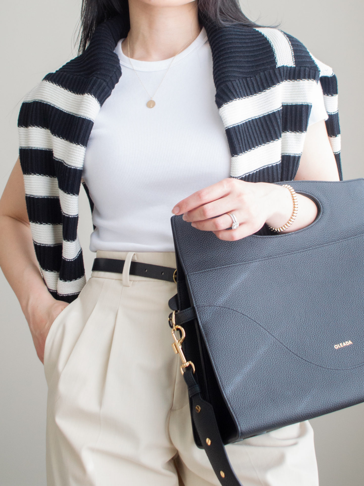 Close up shot of a casual chic outfit worn by Sharon of Her Simple Sole, featuring a black and white stripe sweater over the shoulders, a white ribbed crop t-shirt, cream wide leg pants, gold dainty jewelry, and the Oleada Captain Briefcase in Caviar | casual chic style | minimalist outfit | spring outfit idea