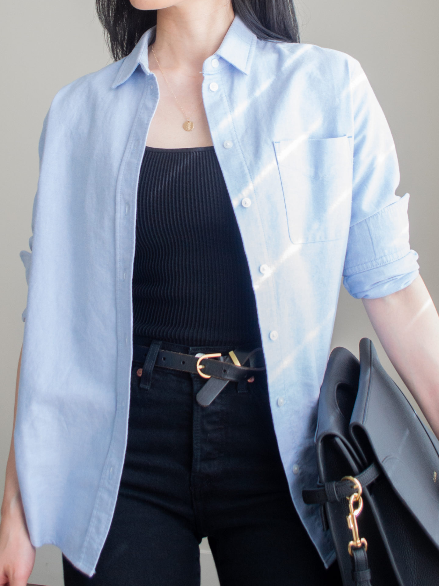 Close up shot of a casual chic outfit worn by Sharon of Her Simple Sole featuring a blue relaxed oxford shirt, black straight leg jeans, a ribbed square neck tank top, gold dainty jewelry, and the Oleada Captain Briefcase bag in Caviar | casual outfit idea | minimalist outfit | spring outfit idea