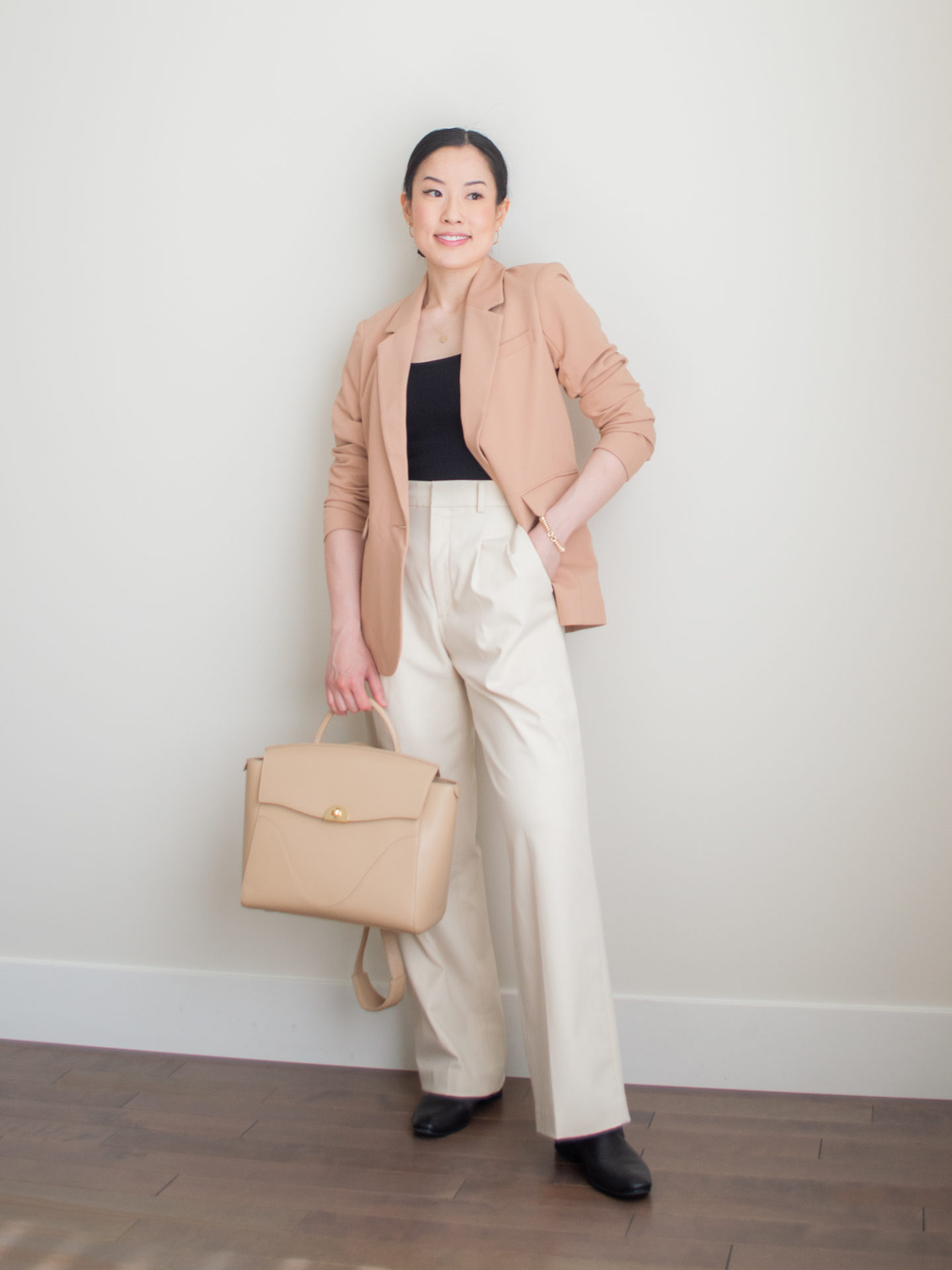 A casual chic outfit worn by Sharon of Her Simple Sole, featuring a brown classic blazer in a petite fit, a black ribbed square neck tank top, cream wide leg pants, classic black loafers, gold dainty jewelry, and the Oleada Wavia bag in Champagne | workwear outfits | minimalist outfit | spring outfit idea