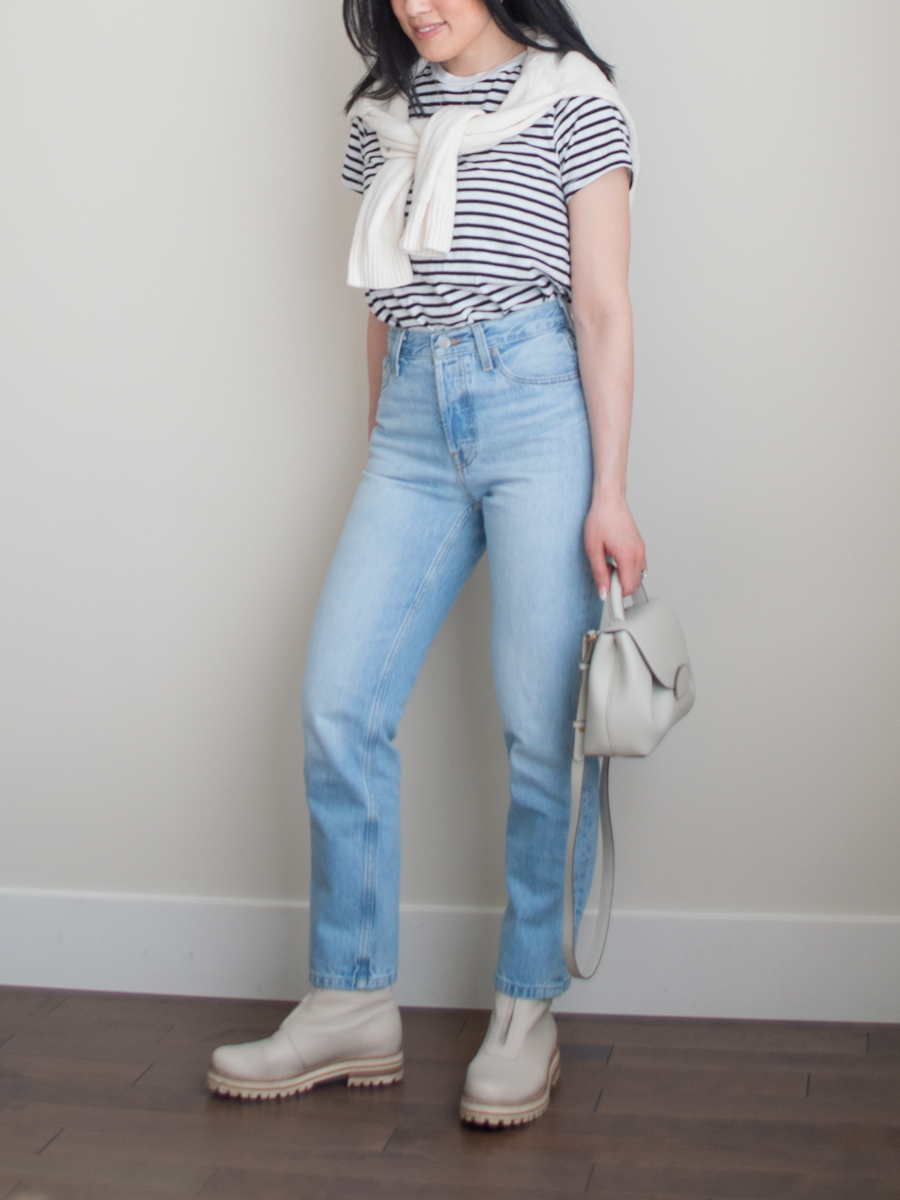 Intentional Life & Style Content Creator Sharon of Her Simple Sole is wearing a minimal spring outfit featuring a knit sweater over the shoulders, a striped black and white t-shirt, light wash blue jeans, and an off-white crossbody bag | simple styling tips | smart casual outfit | the three color rule | the third piece rule | fashion style tips