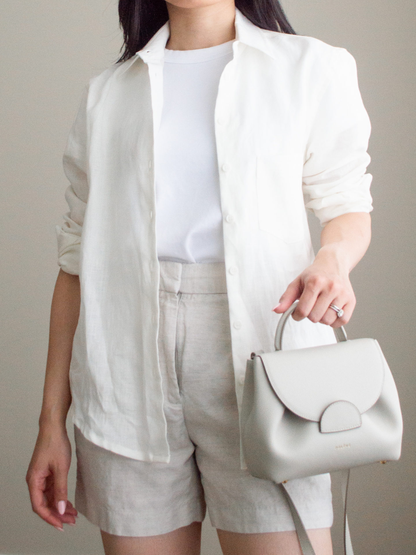 Close-up detailed outfit shot of Sharon of Her Simple Sole wearing a basic white t-shirt, a linen long-sleeve shirt, and linen shorts, while holding a Polene bag | minimalist outfit ideas | light toned outfit