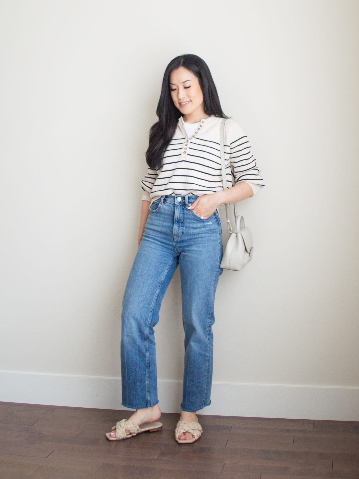 Sharon of Her Simple Sole is wearing items from her list of 10 summer wardrobe essentials, including a striped cotton sweater, a basic white tank top underneath, and blue straight leg jeans, while holding a Polene bag | minimalist outfit ideas | striped sweater and jeans outfit