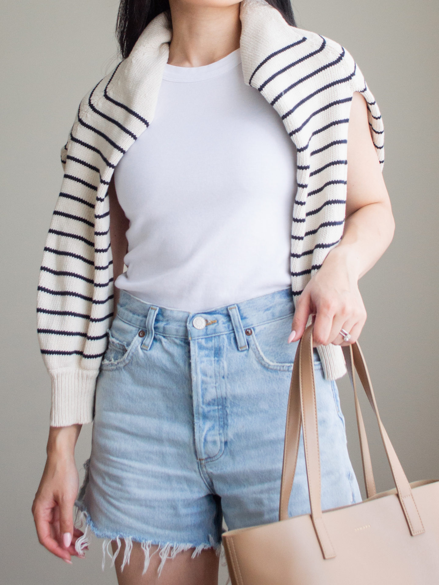 Close-up detailed outfit shot of Sharon of Her Simple Sole wearing a basic cotton tank top, a striped sweater over the shoulders, and relaxed denim shorts, while holding a brown tote bag | minimalist outfit ideas | tank top and denim shorts outfit