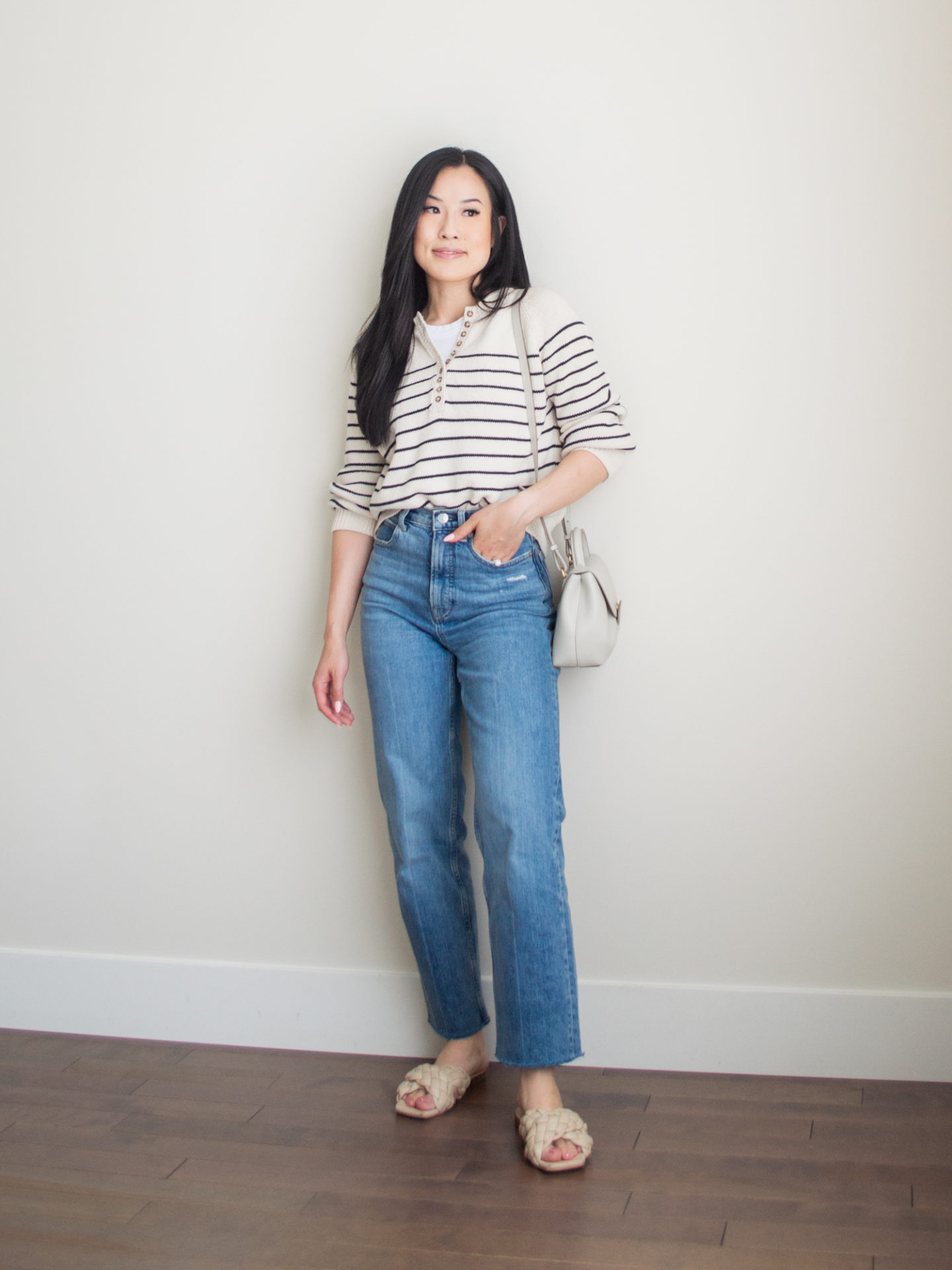 Sharon of Her Simple Sole is wearing items from her list of 10 summer wardrobe essentials, including a striped cotton sweater, a basic white tank top underneath, and blue straight leg jeans, while holding a Polene bag | minimalist outfit ideas | striped sweater and jeans outfit