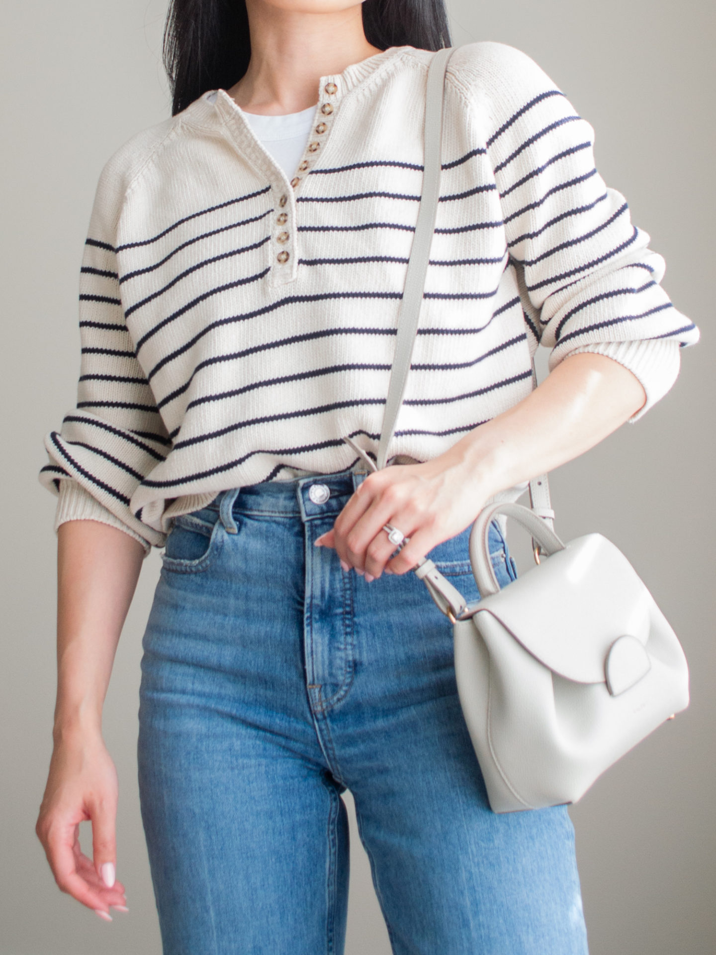 Close-up detailed outfit shot of Sharon of Her Simple Sole wearing a striped cotton sweater, a basic white tank top underneath, and blue straight leg jeans, while holding a Polene bag | minimalist outfit ideas | striped sweater and jeans outfit