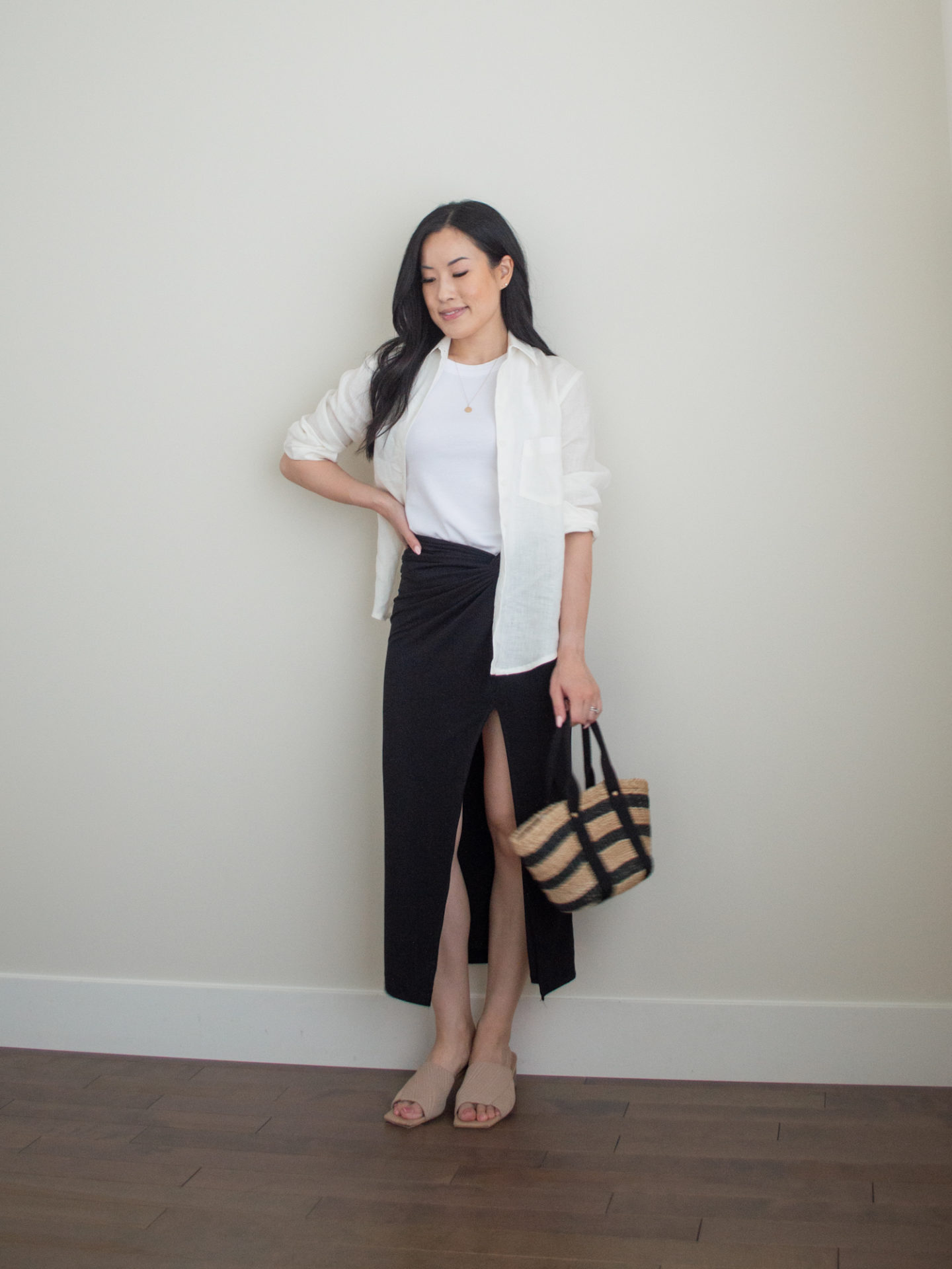 Sharon of Her Simple Sole is wearing an outfit using tips on how to elevate basic summer wardrobe essentials, including a basic white tank top, a linen long-sleeve shirt, a black midi skirt while holding a brown straw bag with black stripes and wearing neutral open toe mules | minimalist outfit ideas | basic summer wardrobe essentials