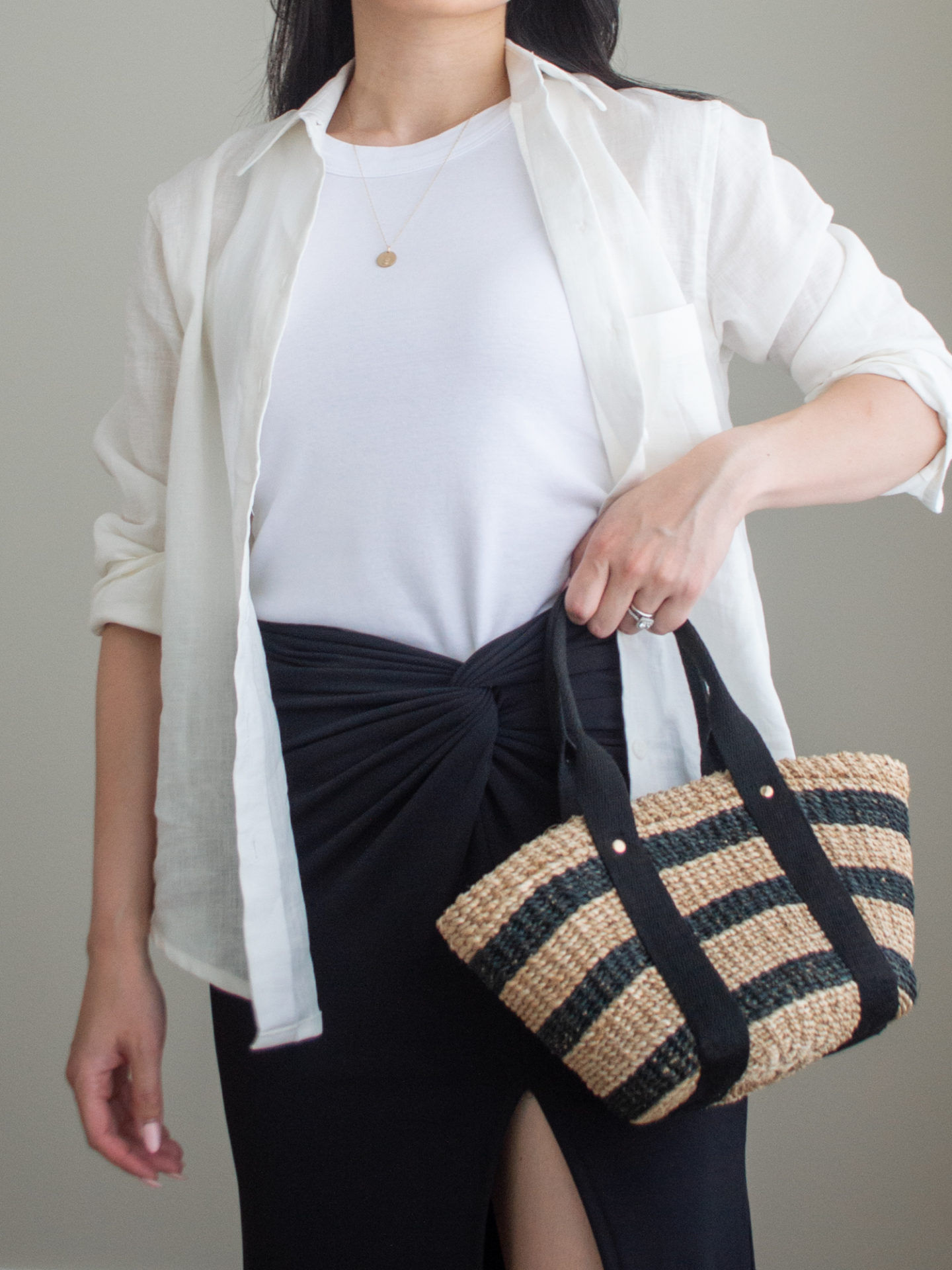 Close-up detailed outfit shot of Sharon of Her Simple Sole wearing a basic white tank top, a linen long-sleeve shirt, a black midi skirt while holding a brown straw bag with black stripes | minimalist outfit ideas | linen shirt outfit