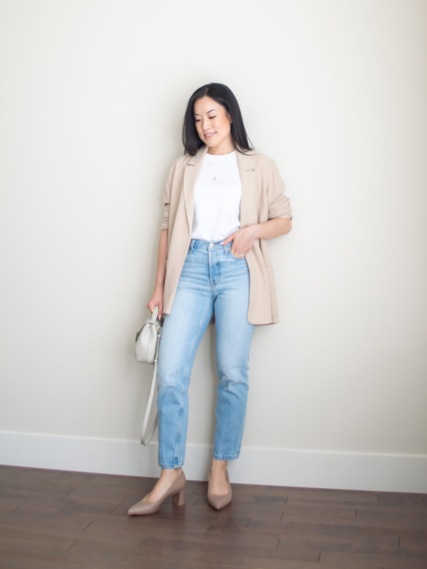 Sharon of Her Simple Sole is wearing an outfit from her blog post about How to Style Smart Casual Outfits Using the 2×2 Outfit Formula, featuring a white basic t-shirt, blue straight leg jeans, a flowy linen blend blazer, and block heels from Ally Shoes, while holding an off-white crossbody bag | minimalist outfit ideas | smart casual outfits | 2x2 outfit formula | comfortable pumps