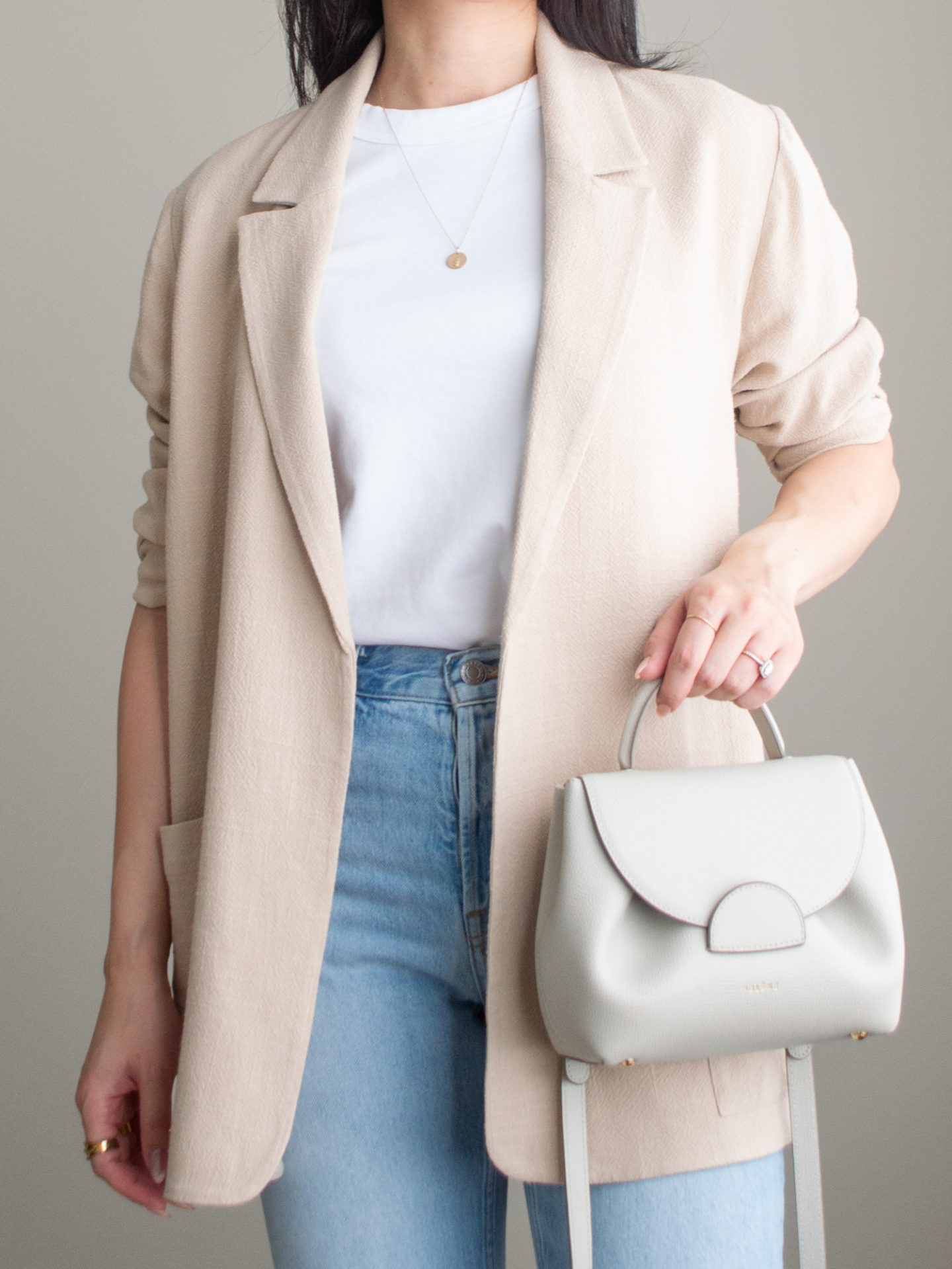 Close-up detailed outfit shot of Sharon of Her Simple Sole wearing a white basic t-shirt, blue straight leg jeans, and a flowy linen blend blazer, while holding an off-white crossbody bag | minimalist outfit ideas | smart casual outfit