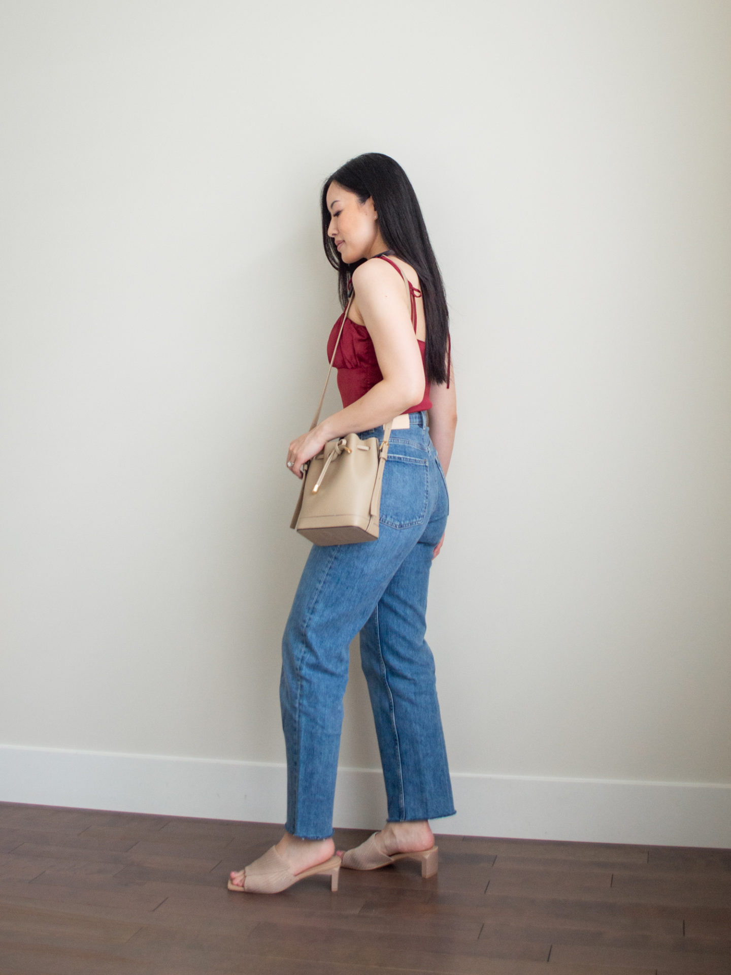 Sharon of Her Simple Sole is wearing a red balconette and blue straight leg jeans, while holding a taupe bucket bag bag and wearing neutral open toe mules | minimalist outfit ideas | straight led jean |