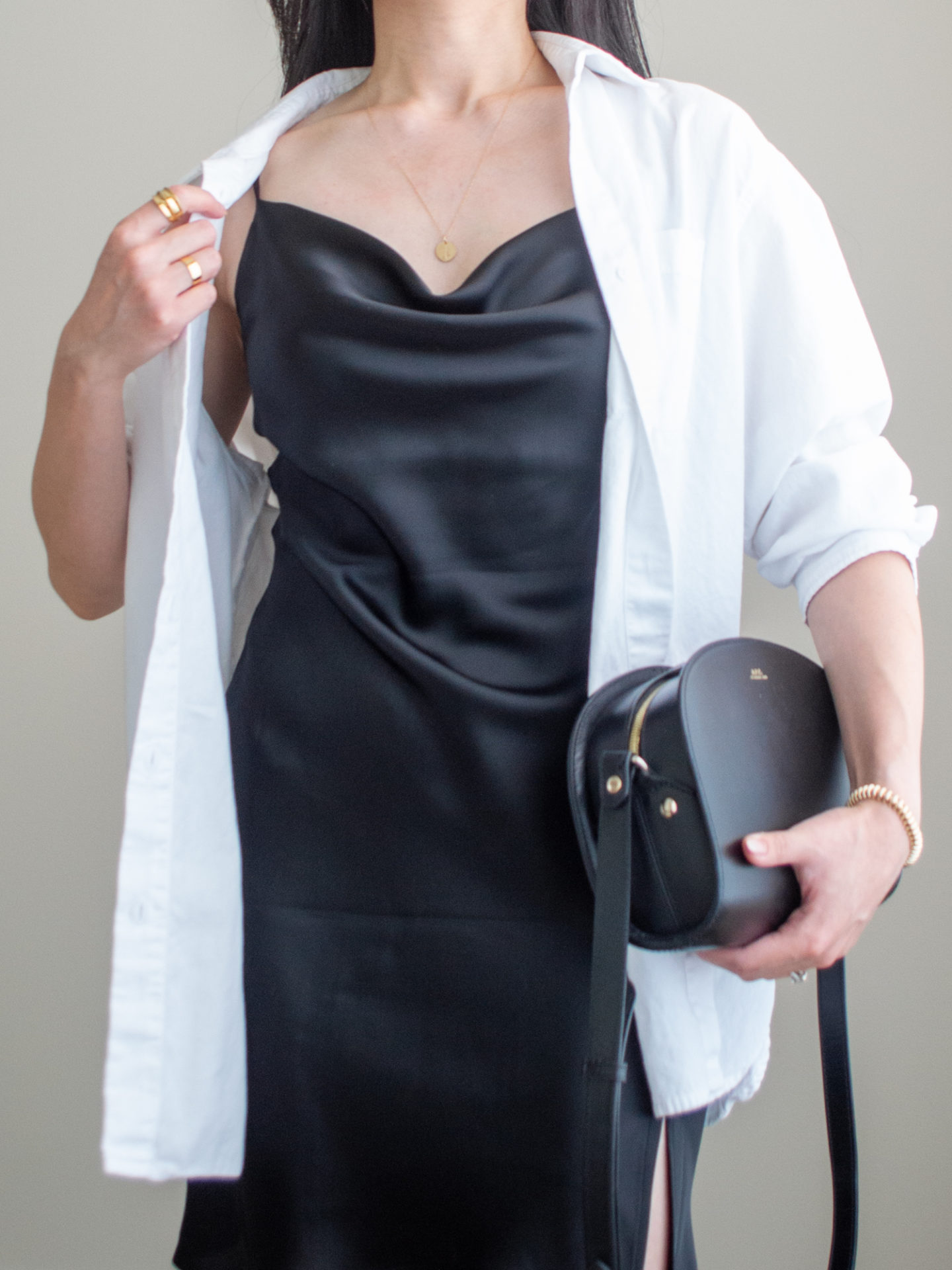 Close-up detailed outfit shot of Sharon of Her Simple Sole wearing a black cowl neck mini slip dress, with an oversized white button-up shirt while holding a black crossbody bag | minimalist outfit ideas | summer date night outfits