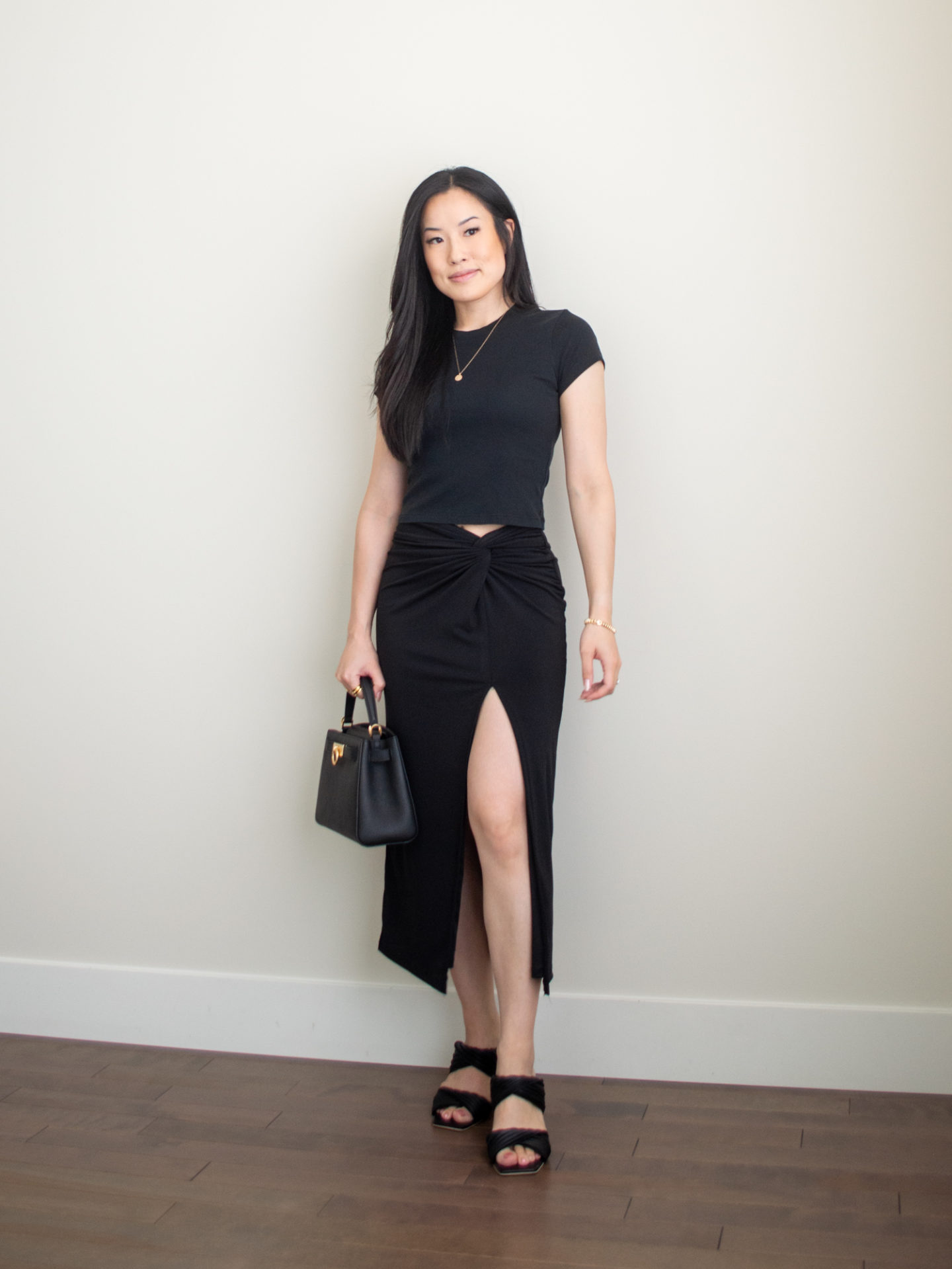 Sharon of Her Simple Sole is wearing an outfit from her 5 Simple Summer Date Night Outfits blog post featuring a black baby t-shirt, a black midi skirt, while wearing block heeled sandals and holding a black top handle bag | minimalist outfit ideas | summer date night outfits