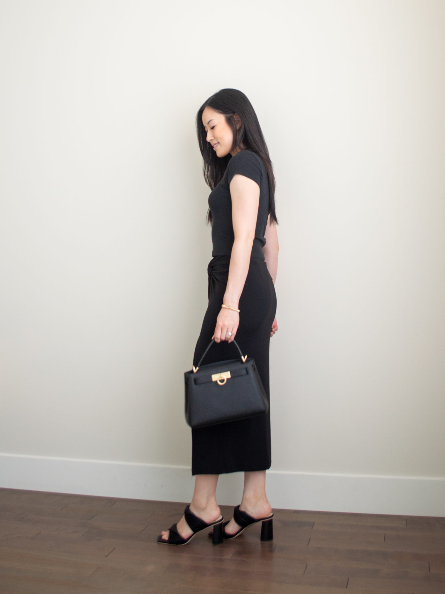 Sharon of Her Simple Sole is wearing a black baby t-shirt, a black midi skirt, while wearing block heeled sandals and holding a black top handle bag | minimalist outfit ideas | black monochrome outfit