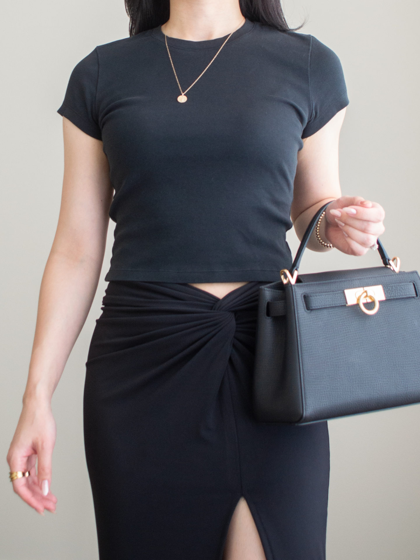 Close-up detailed outfit shot of Sharon of Her Simple Sole wearing a black baby t-shirt and a black midi skirt while holding a black top handle bag and gold jewelry | minimalist outfit ideas | summer date night outfits