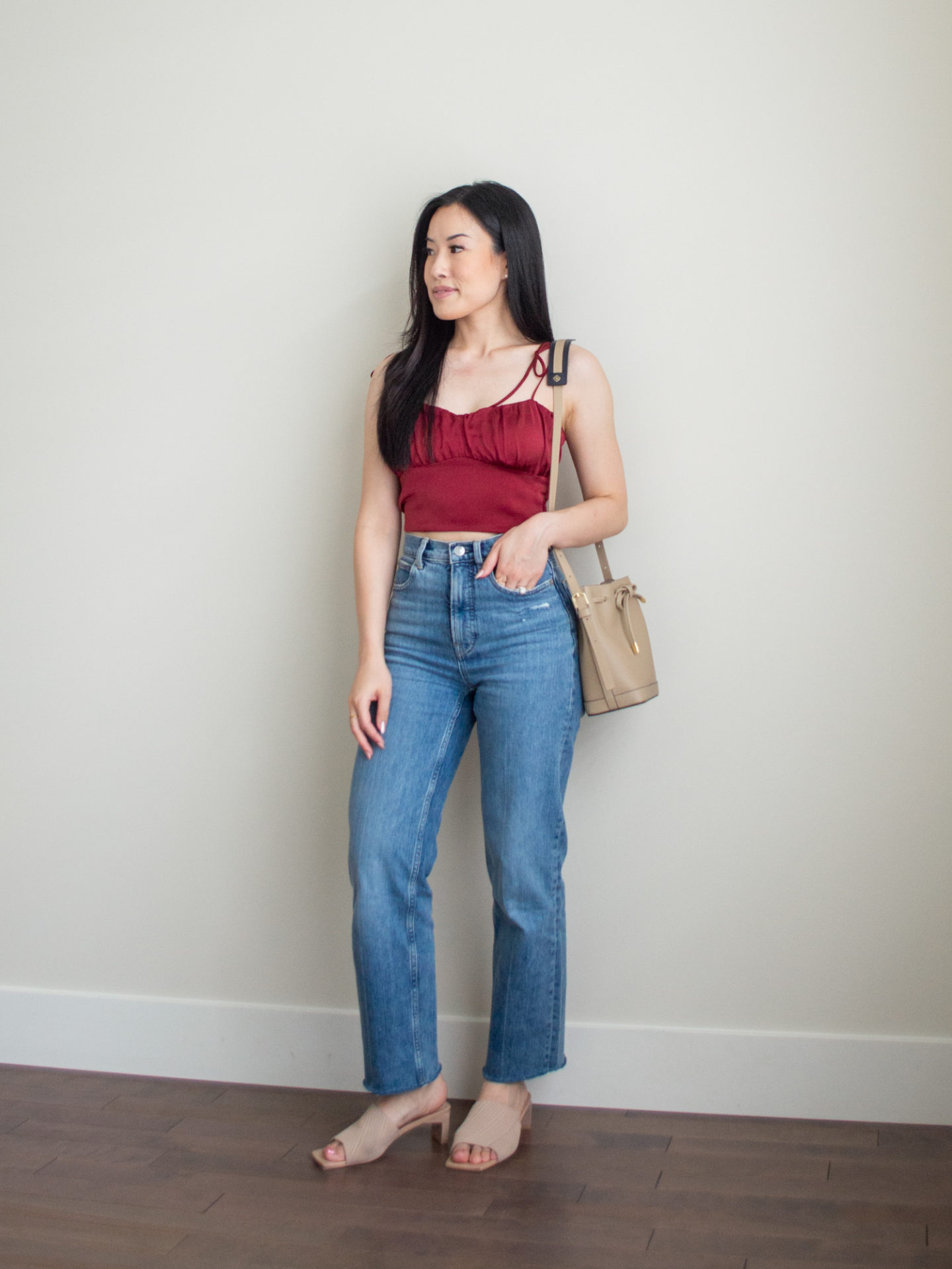 Sharon of Her Simple Sole is wearing an outfit from her 5 Simple Summer Date Night Outfits blog post featuring a red balconette and blue straight leg jeans, while holding a taupe bucket bag bag and wearing neutral open toe mules | minimalist outfit ideas | date night outfits