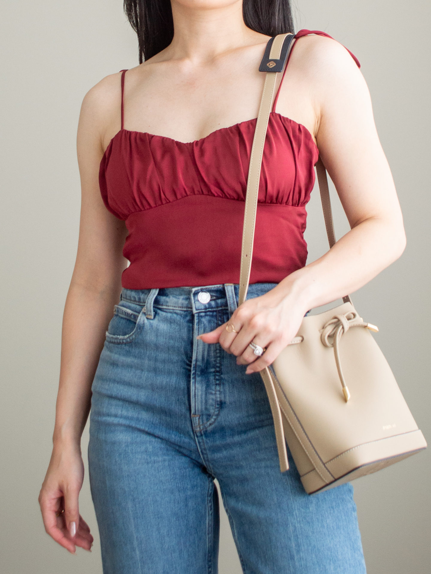 Close-up detailed outfit shot of Sharon of Her Simple Sole wearing a red balconette and blue straight leg jeans, while holding a taupe bucket bag | minimalist outfit ideas | summer date night outfits