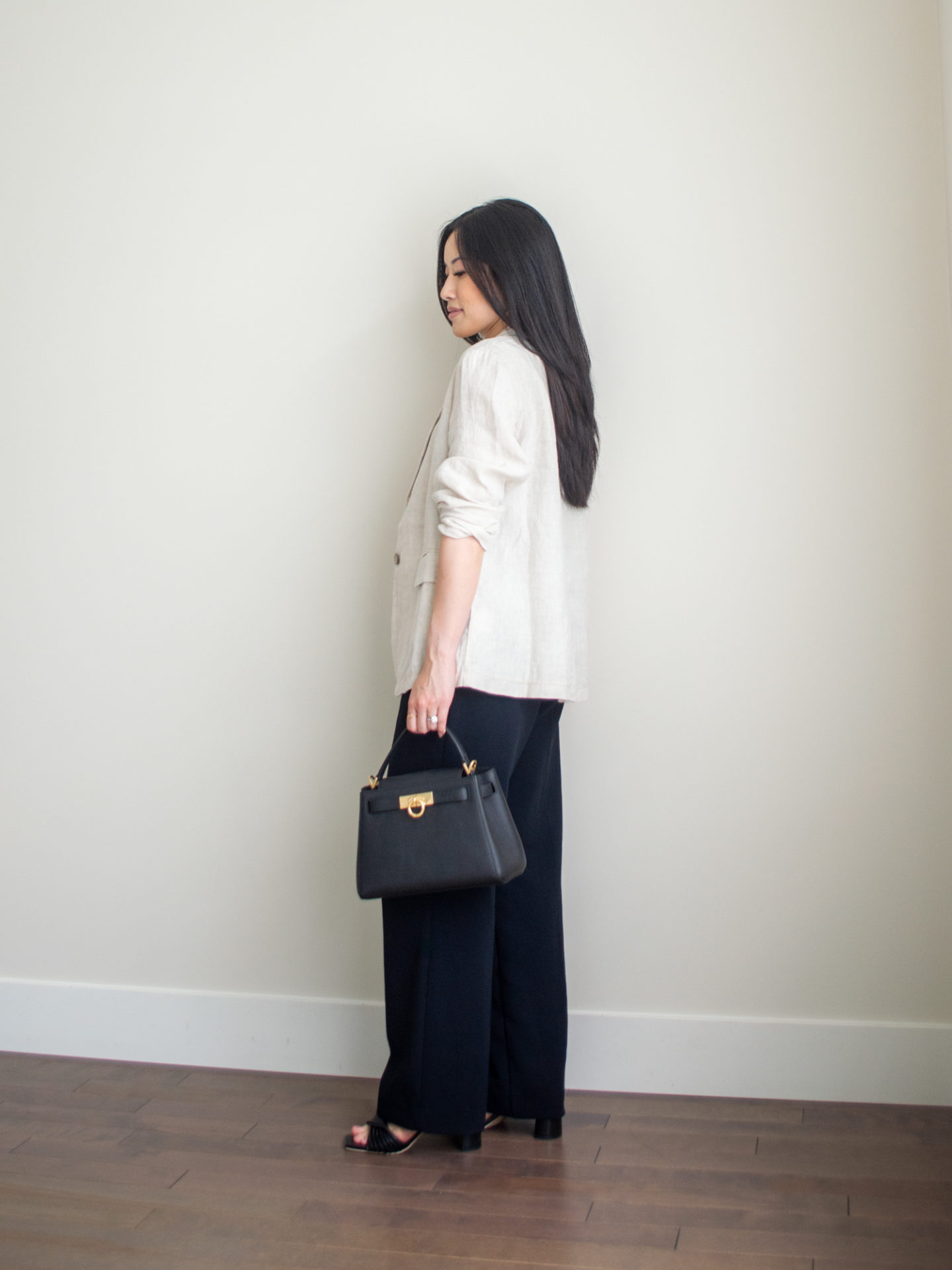 Sharon of Her Simple Sole is wearing a green lace bustier, linen blazer, and black wide leg pants, while holding a black top handle bag and wearing block heeled sandals | minimalist outfit ideas