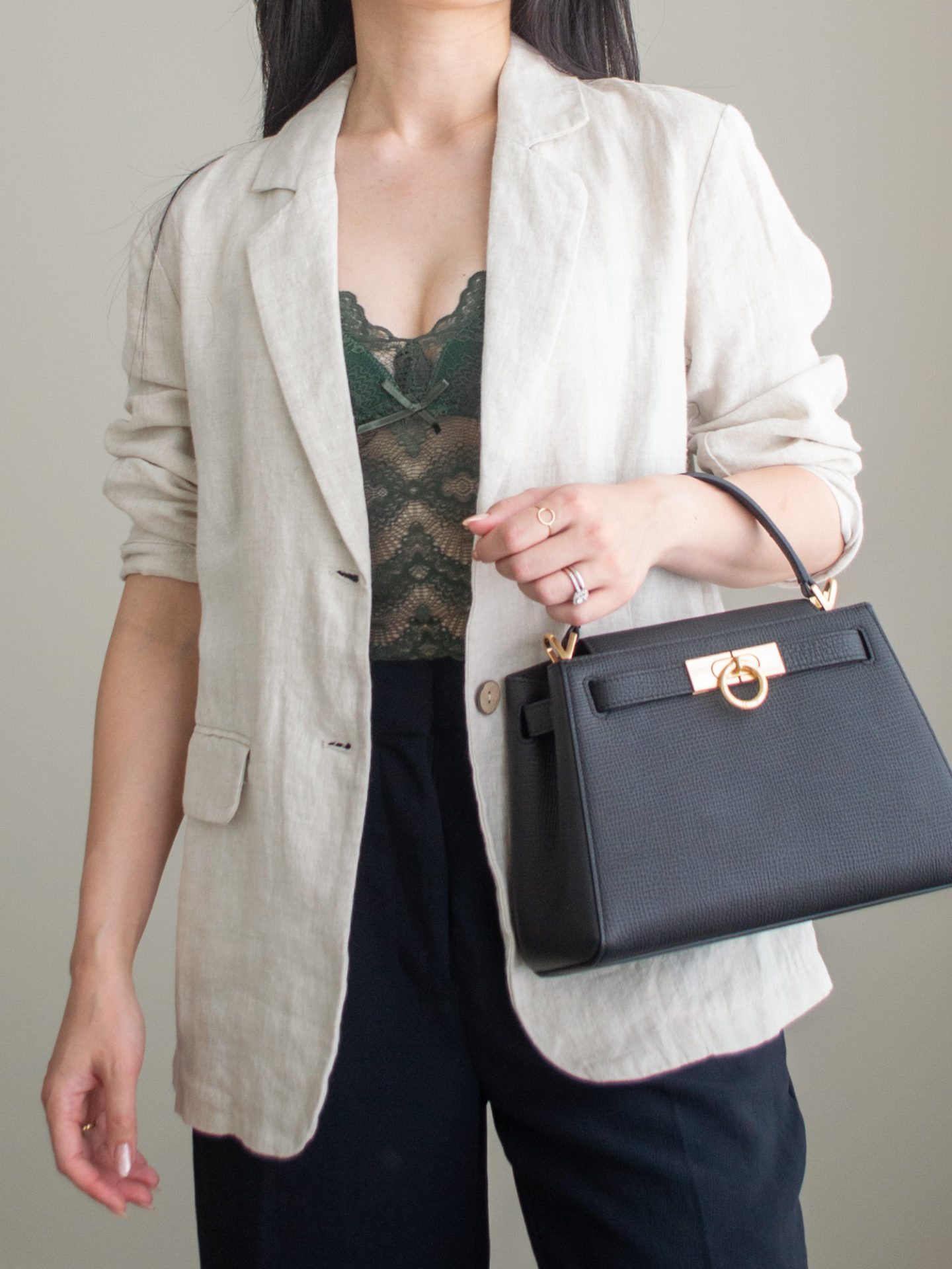 Close-up detailed outfit shot of Sharon of Her Simple Sole wearing a green lace bustier, black wide leg pants, and a linen blazer, while holding a black top handle bag | minimalist outfit ideas | summer date night outfits