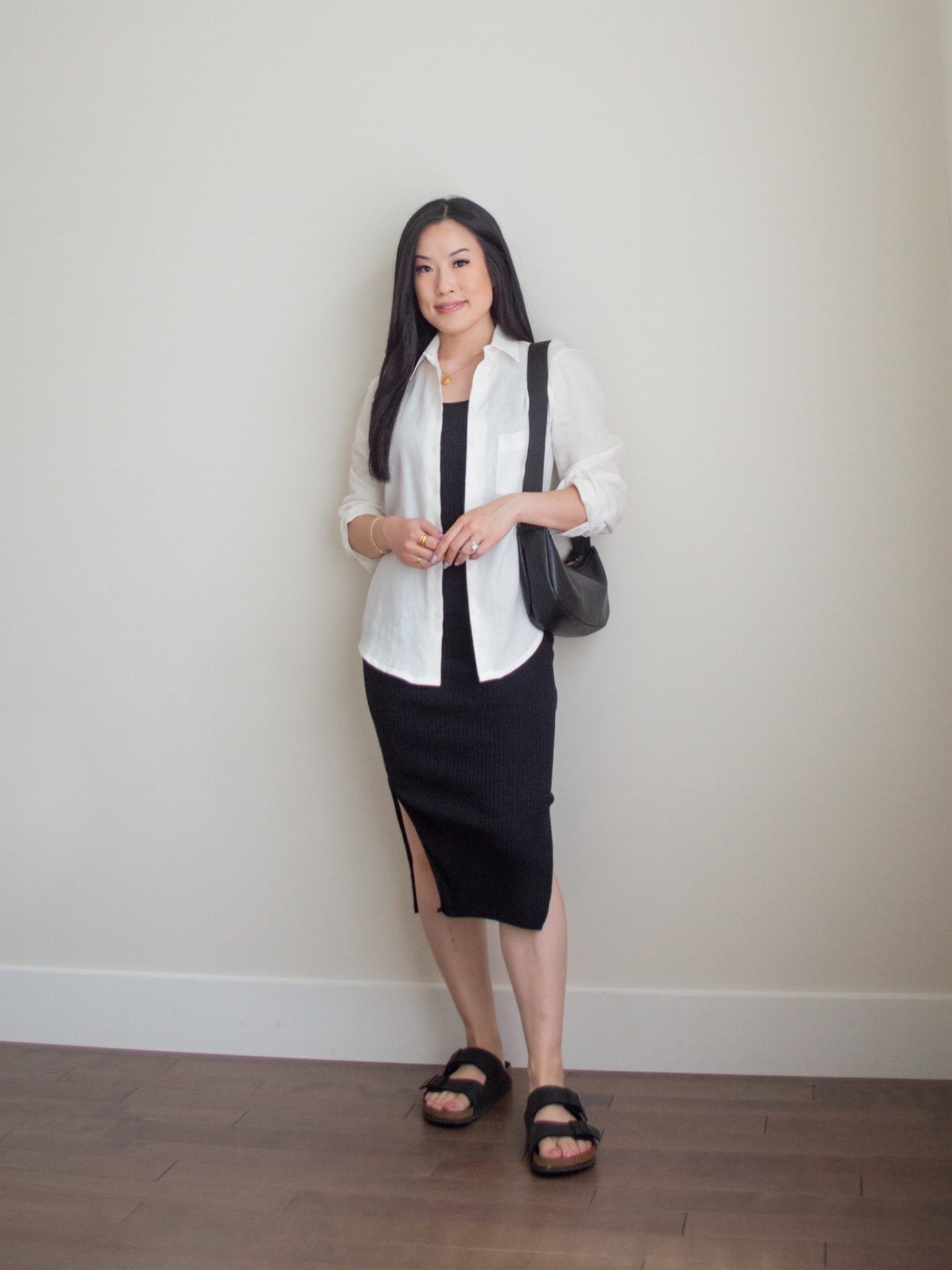 Sharon of Her Simple Sole is wearing an outfit from her June outfit roundup, including a black ribbed midi dress and a long sleeve linen button up shirt, while holding a black slouchy bag and wearing birkenstock sandals | minimalist outfit ideas | summer outfit idea | linen and cotton outfit