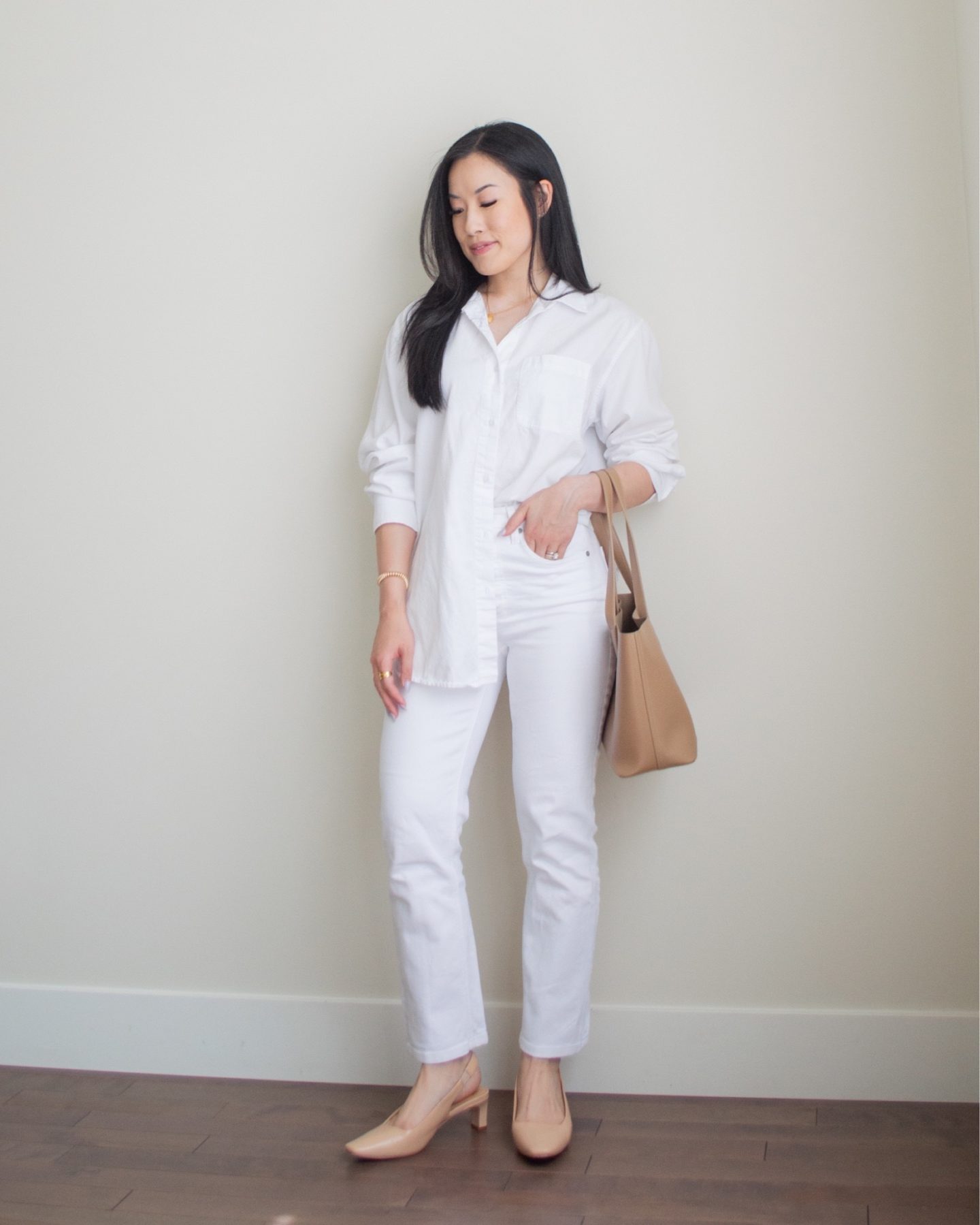 Sharon of Her Simple Sole is wearing a white oversized button up shirt and white straight leg jeans, while holding a caramel coloured mini tote bag and wearing beige sling back heels | minimalist outfit ideas | summer outfit idea | linen and cotton outfit