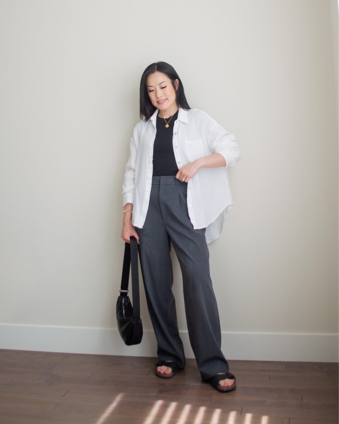 Sharon of Her Simple Sole is wearing an outfit from her June outfit roundup, including an oversized cotton gauze button up shirt, a basic black t-shirt, and grey wide leg pants, while holding a black slouchy bag and wearing birkenstock sandals | minimalist outfit ideas | summer outfit idea