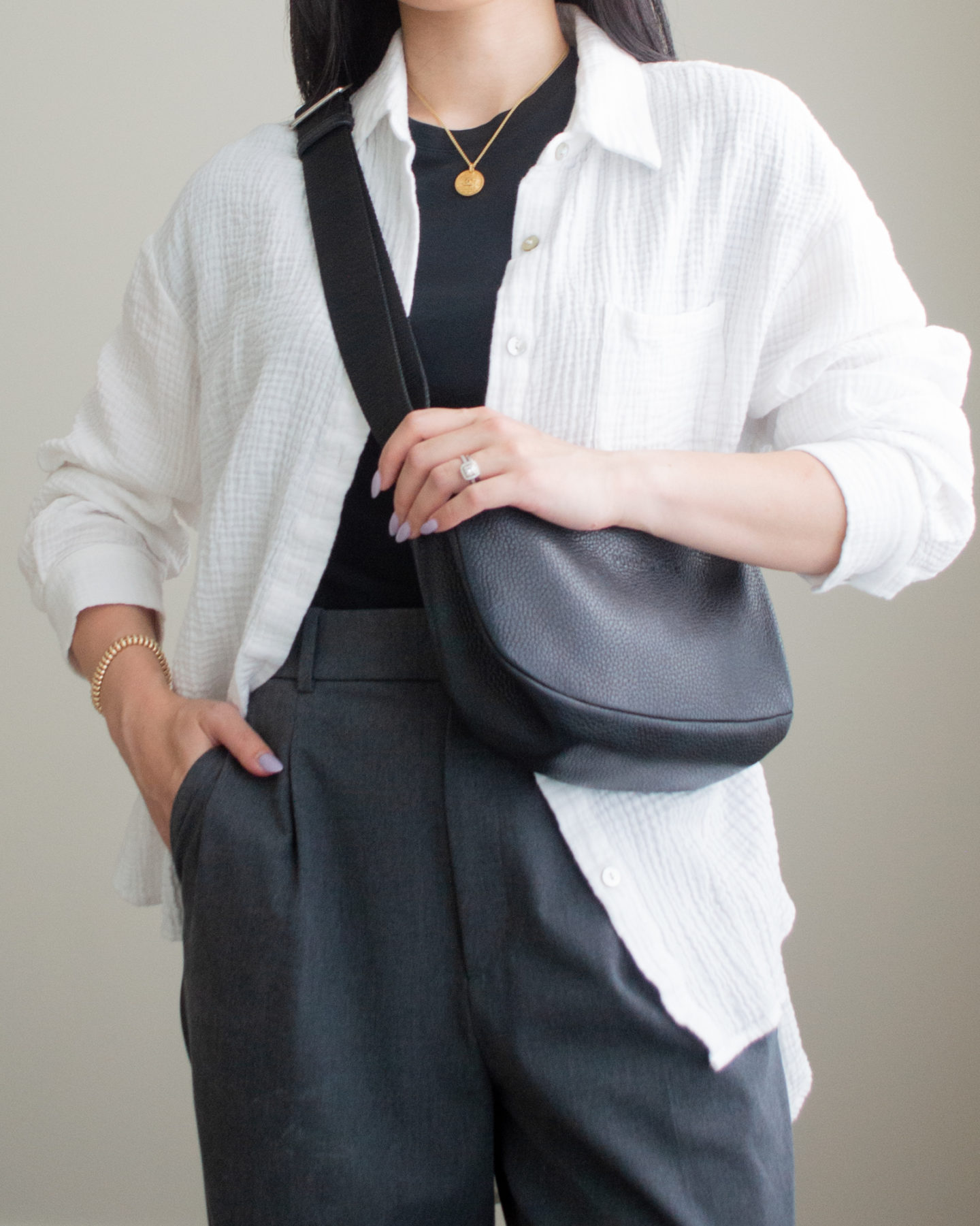 Close-up detailed outfit shot of Sharon of Her Simple Sole wearing an oversized cotton gauze button up shirt, a basic black t-shirt, and grey wide leg pants, while holding a black slouchy bag | minimalist outfit ideas | smart casual outfit