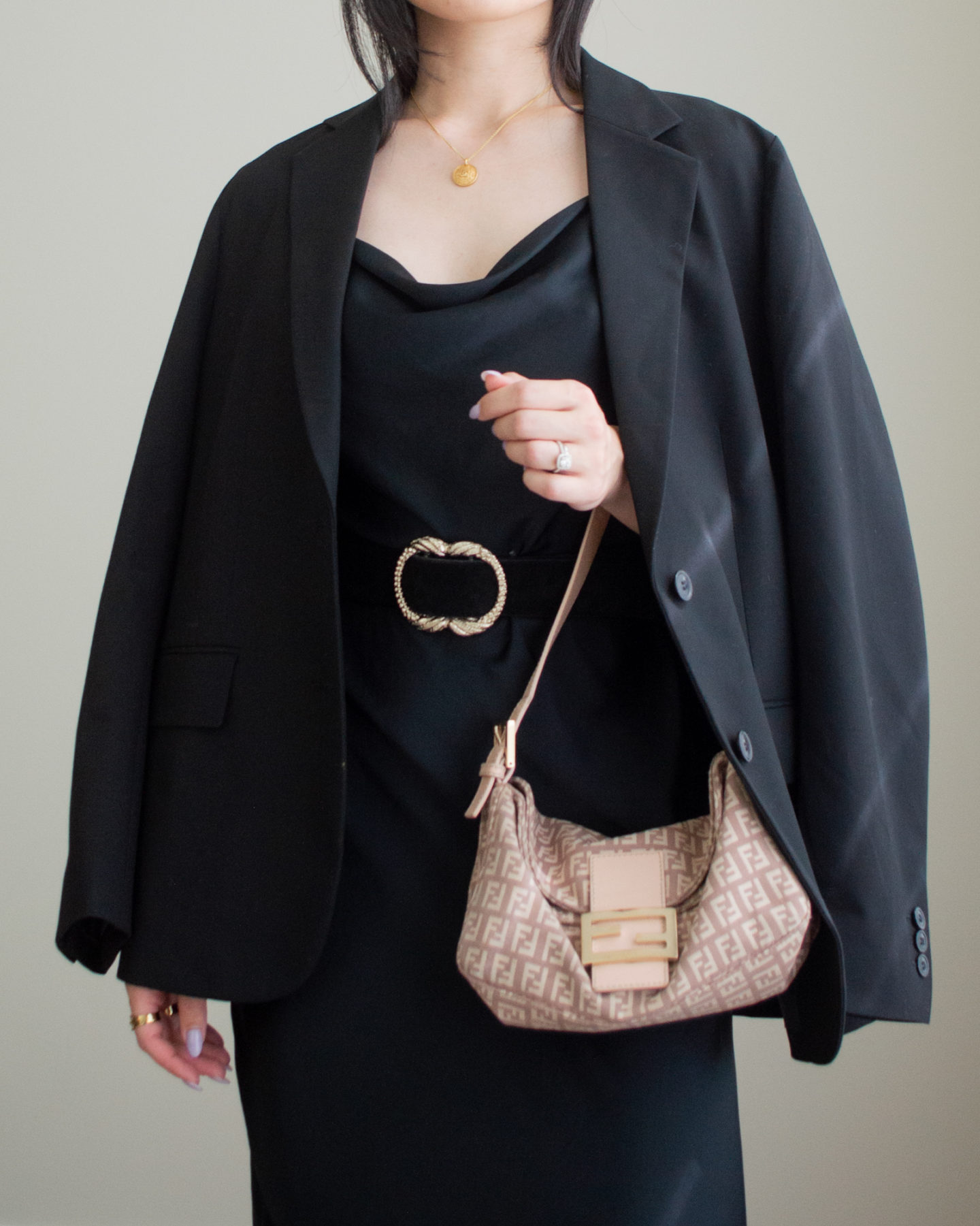 Close-up detailed outfit shot of Sharon of Her Simple Sole wearing a black oversized blazer, a black cowl neck midi slip dress, a statement belt tied around the waist, and a Fendi baguette bag | minimalist outfit ideas | simple wedding guest outfit