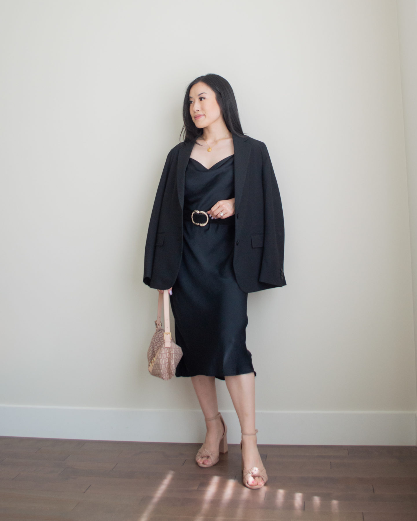 Sharon of Her Simple Sole is wearing a black oversized blazer, a black cowl neck midi slip dress, a statement belt tied around the waist, blush pink bow heeled sandals, and a Fendi baguette bag | minimalist outfit ideas | summer outfit idea | linen and cotton outfit