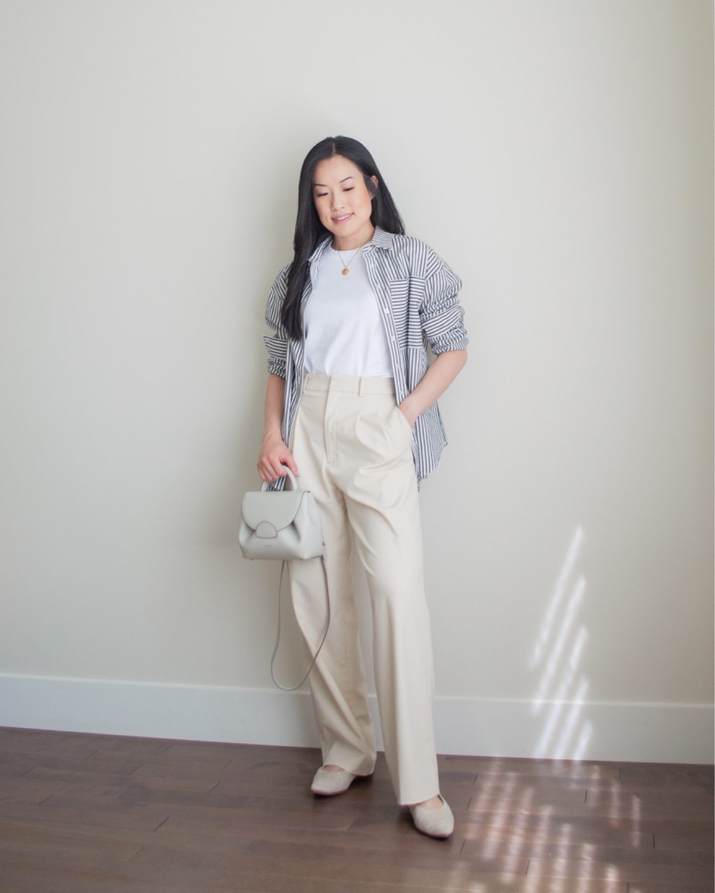 Sharon of Her Simple Sole is wearing an outfit from her June outfit roundup, including a striped button up shirt, a basic white t-shirt, and cream wide leg pants, while holding a Polene crossbody bag and wearing pointy toe flats | minimalist outfit ideas | tshirt and wide leg pants outfit