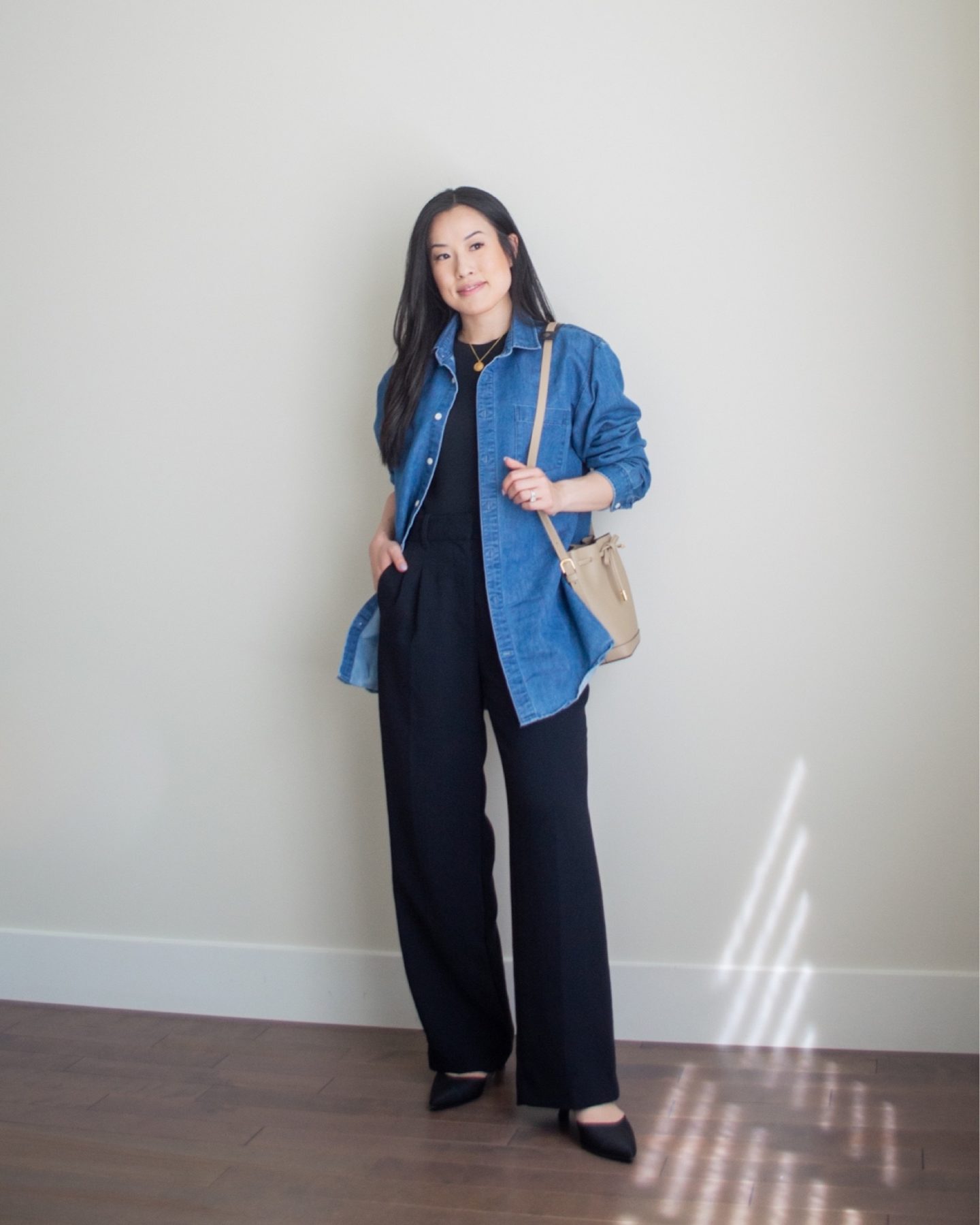 Sharon of Her Simple Sole is wearing a basic black t-shirt, a denim button up shirt, and black wide leg pants, while holding a taupe bucket bag and wearing black sling back kitten heels | minimalist outfit ideas | smart casual outfit | tshirt and wide leg pants outfit