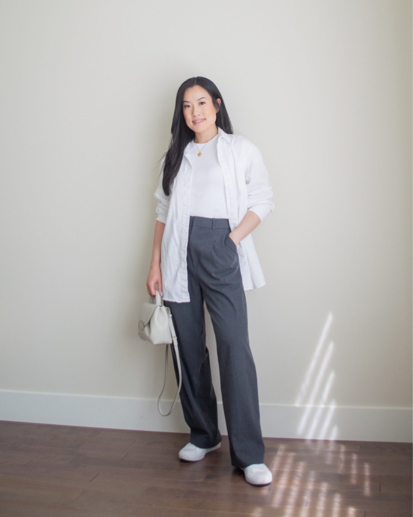 Sharon of Her Simple Sole is wearing an outfit from her June outfit roundup, including a white baby t-shirt, an oversized white button up shirt, and grey wide leg pants, while holding a Polene crossbody bag and wearing white sneakers | minimalist outfit ideas | smart casual outfit | tshirt and wide leg pants outfit