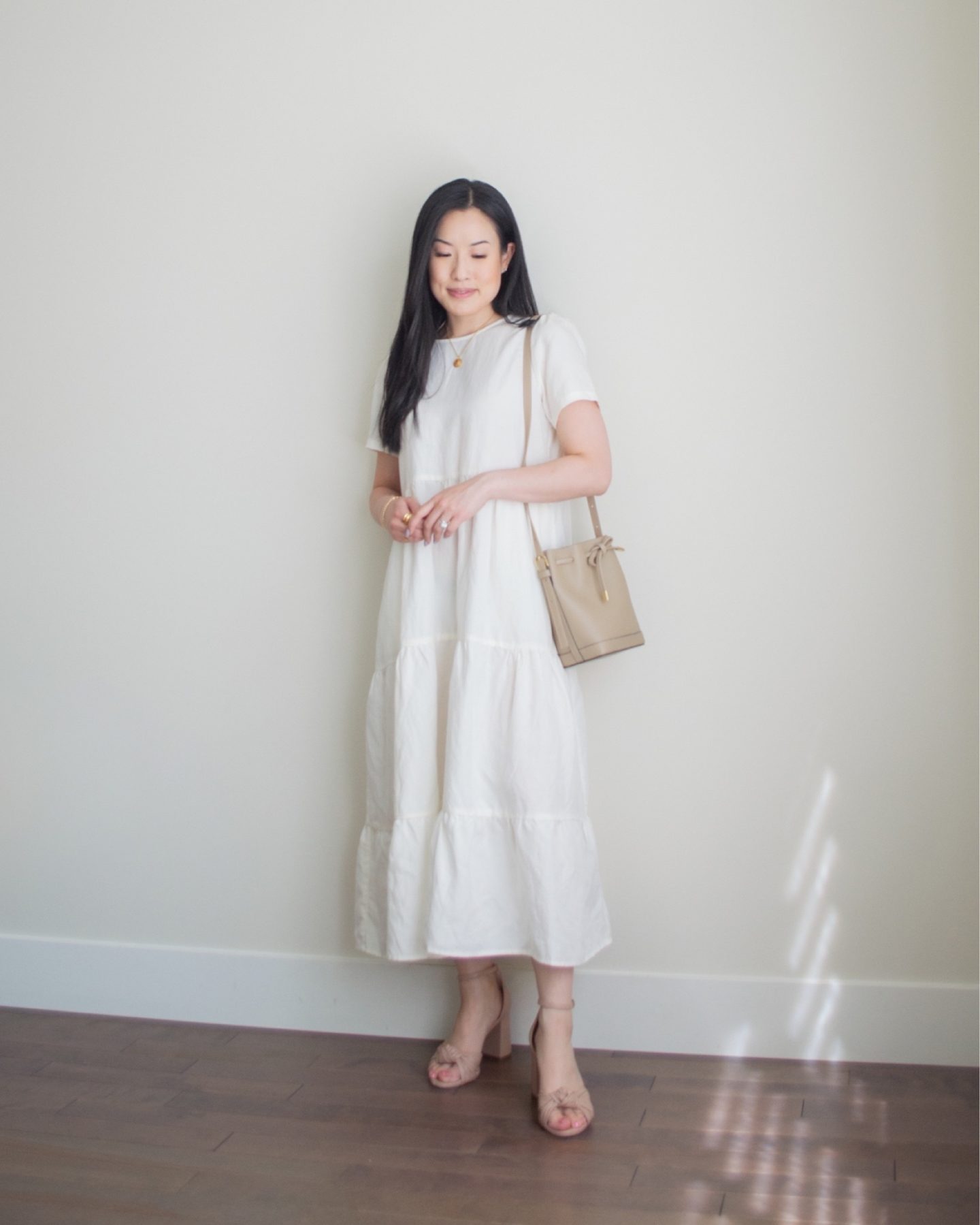 Sharon of Her Simple Sole is wearing a white tiered midi dress, blush bow heeled sandals, a taupe bucket bag and gold jewelry | minimalist outfit ideas | summer dress outfit