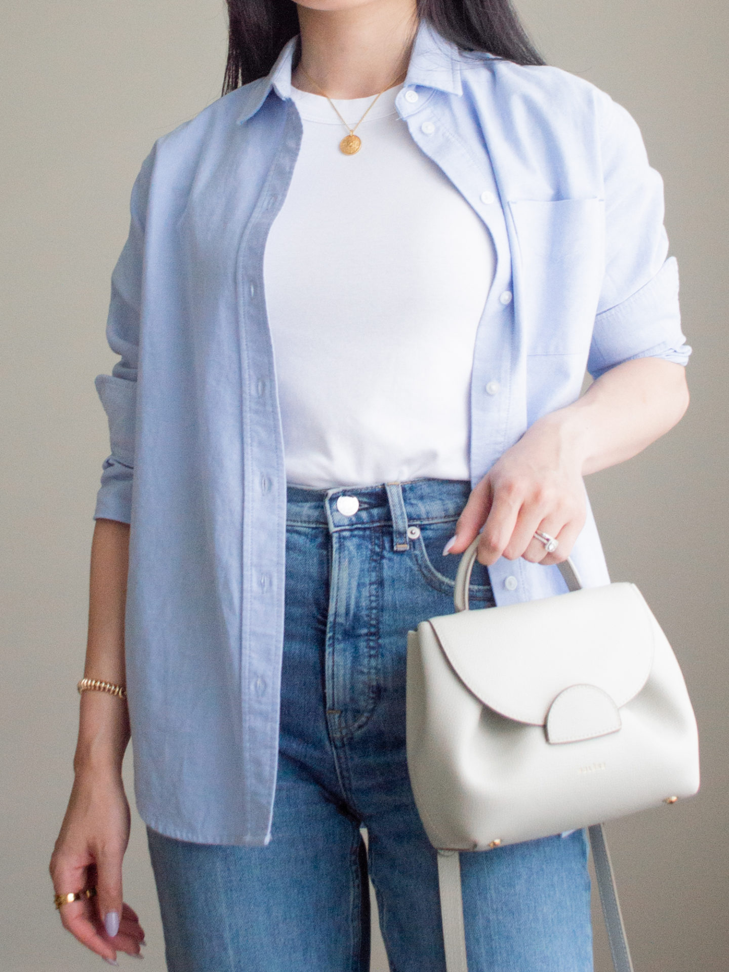 Close-up detailed outfit shot of Sharon of Her Simple Sole wearing a basic cotton tank top, a blue relaxed oxford button up shirt, and blue straight leg jeans, while holding a Polene crossbody bag | minimalist outfit ideas | smart casual outfit