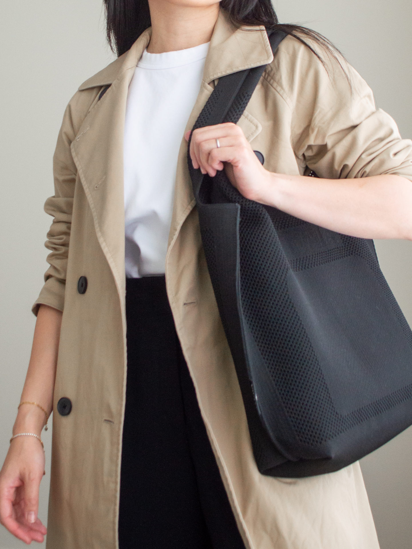 Close-up detailed outfit shot of Sharon of Her Simple Sole wearing a simple white T-shirt, brown trench coat, and black cropped trousers, while holding a black tote bag | minimalist outfits | fall outfit ideas